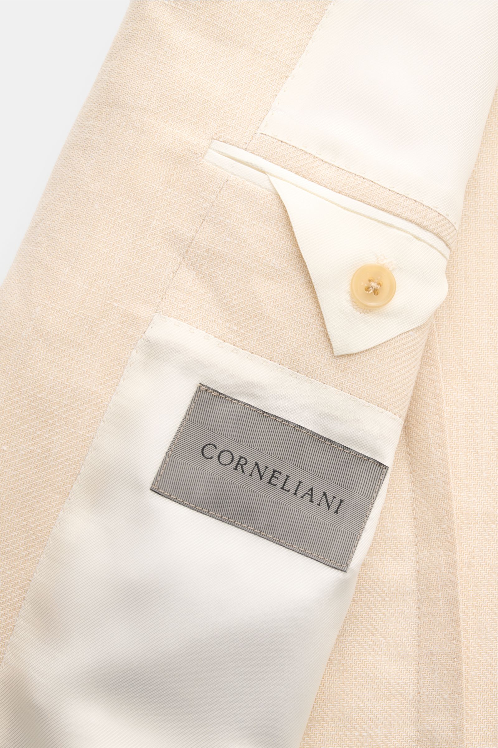 Close-up inside view of Corneliani Sakko creme showing label, button, and fabric texture from a top-down perspective, crafted from Lyocell and linen with soft touch and fine weave.  

Formvollendeter Stil von CORNELIANI: mit optimalem Fit aus italienis