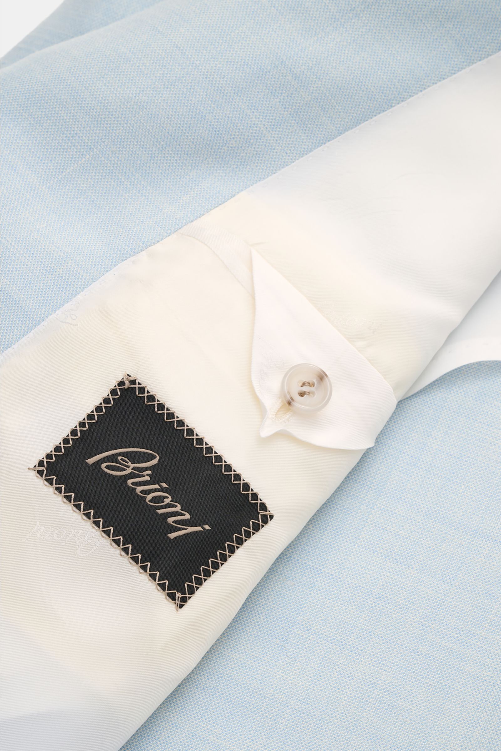 Close-up interior view of Brioni Smart-casual jacket 'Amalfi' pastel blue mottled, showcasing the cream lining, button, and branded label. A confident choice for stylish looks: The exquisite wool-silk blend, refined with linen to create the perfect temper