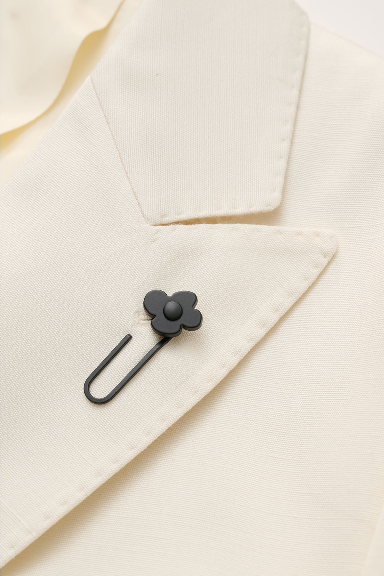 Nahaufnahme des Lardini Sakko creme mit spitzem Revers und schwarzem Blüten-Anstecker, feine Viskose-Seide-Struktur sichtbar.