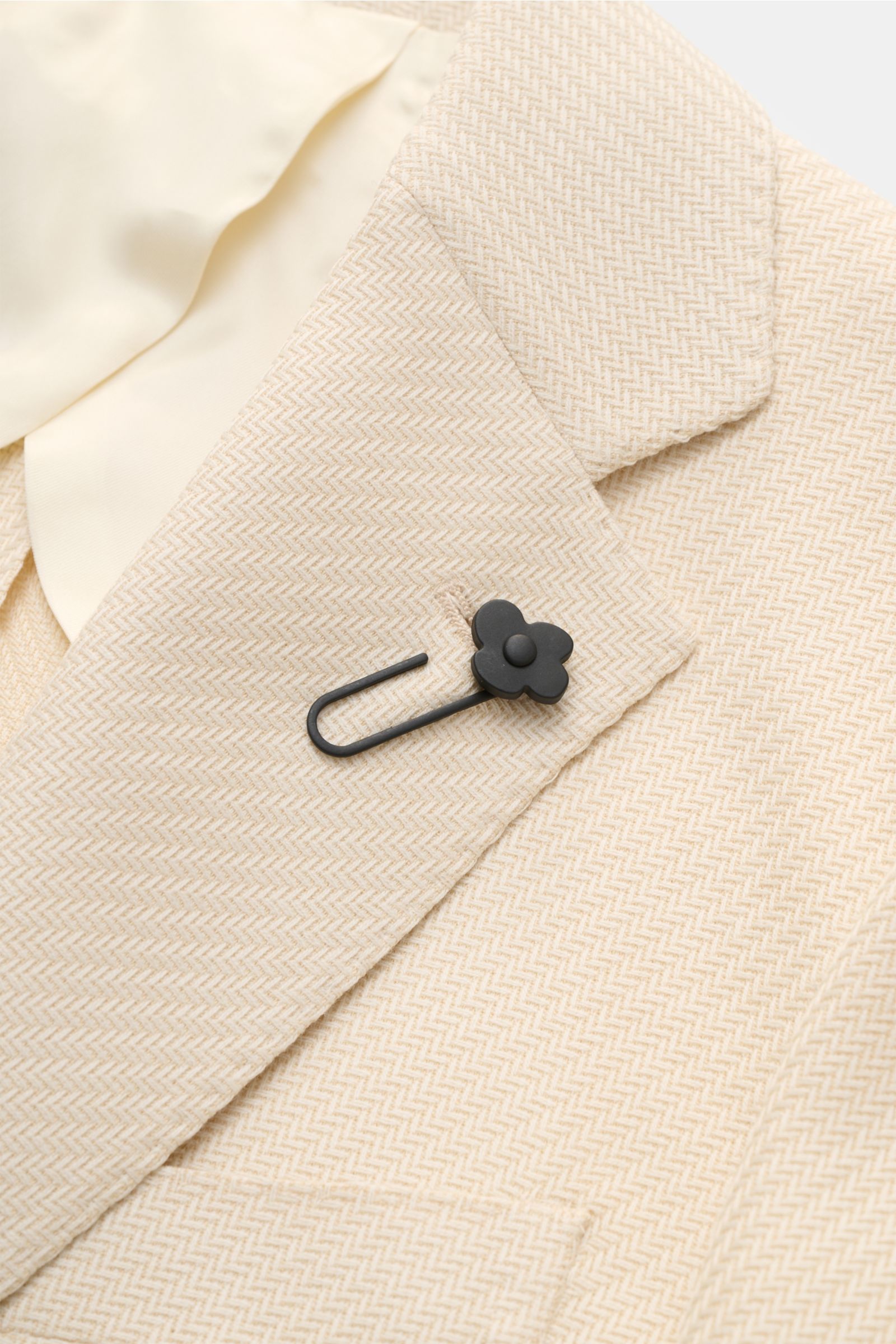 Close-up front view of Lardini Smart-casual jacket cream showing tonal herringbone pattern, step lapel with black flower pin, and soft wool-cotton blend fabric.

An Italian design classic: This smart-casual jacket from LARDINI made of wool and cotton f
