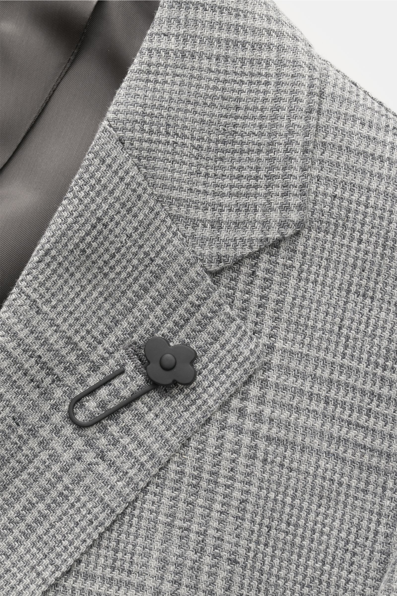 Lardini Sakko grau/hellgrau kariert, Detailaufnahme von schräg oben auf Revers, Blüten-Anstecker und Webstruktur aus Leinen-Woll-Mix.