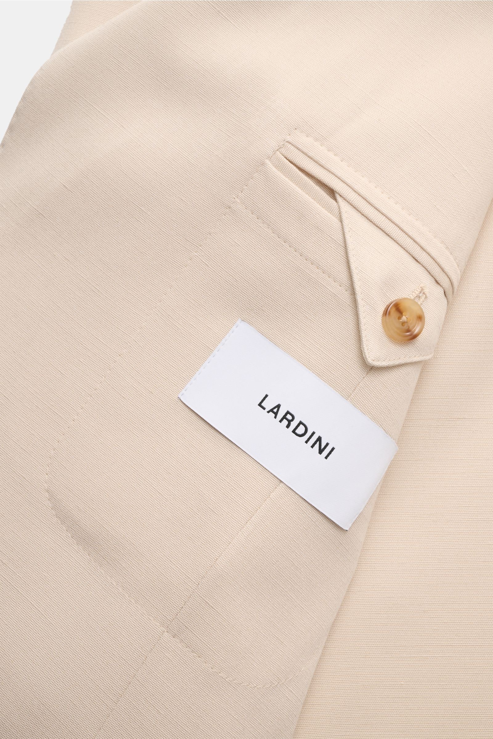 Nahaufnahme des Lardini Sakko sand, fotografiert von schräg oben, zeigt die feine Viskose-Seidenstruktur, Brusttasche mit Knopf und weißen Lardini-Label.
