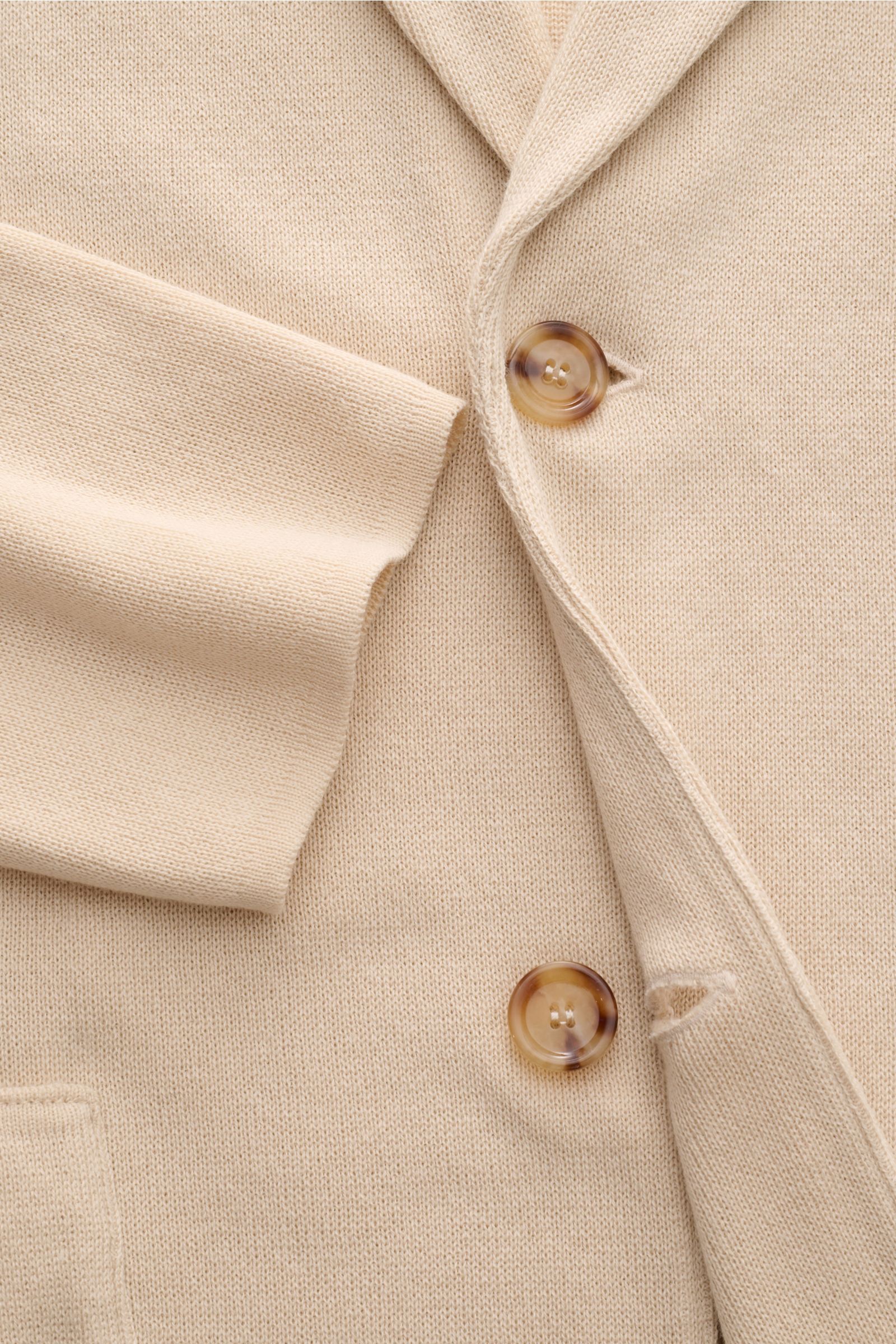 Lardini Strickblazer creme aus reiner Baumwolle, Slim Fit, feines Strickbild, zwei braune Knöpfe, fallendes Revers mit Blüten-Anstecker, Detailaufnahme frontal.
