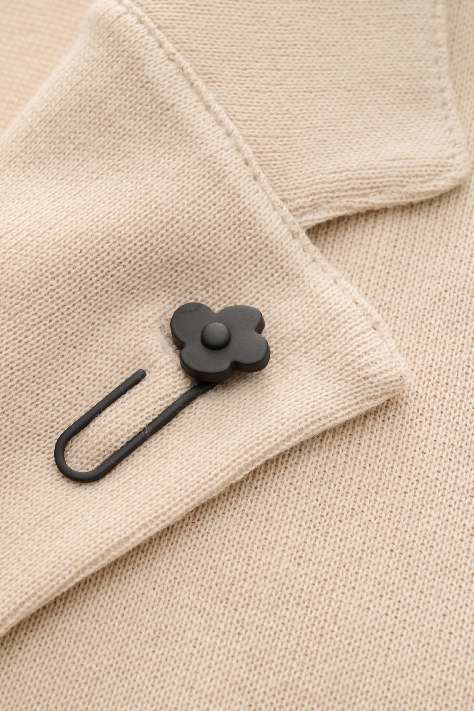 Nahaufnahme des fallenden Revers mit schwarzem Blüten-Anstecker am Lardini Strickblazer creme aus feinem, weichem Baumwollstrick.