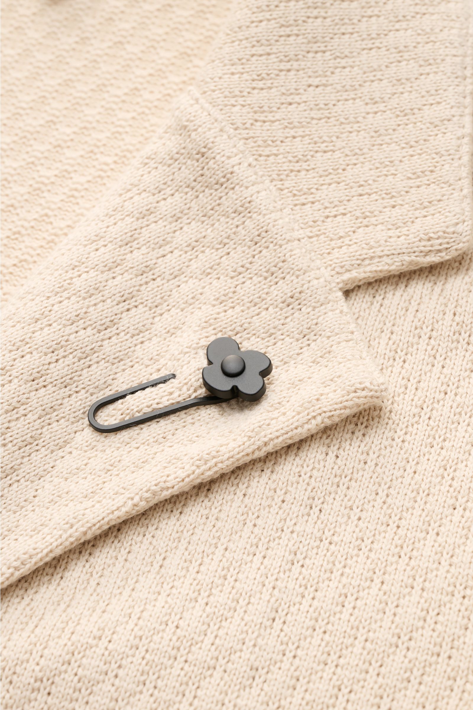 Lardini Strickblazer beige in Nahaufnahme von oben, zwei-Knopf-Stil, fallendes Revers mit Blütenpin, reine Baumwolle, markantes Strickmuster.