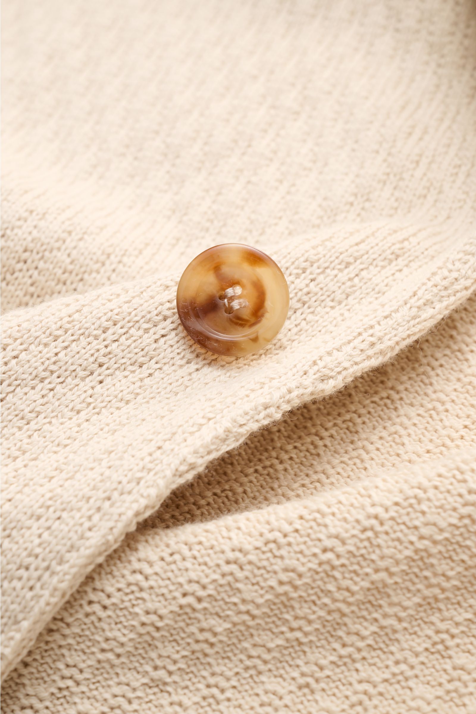 Nahaufnahme des beigen Lardini Strickblazers aus reiner Baumwolle mit markantem Strickmuster und braunem Knopf, Detailfoto frontal.