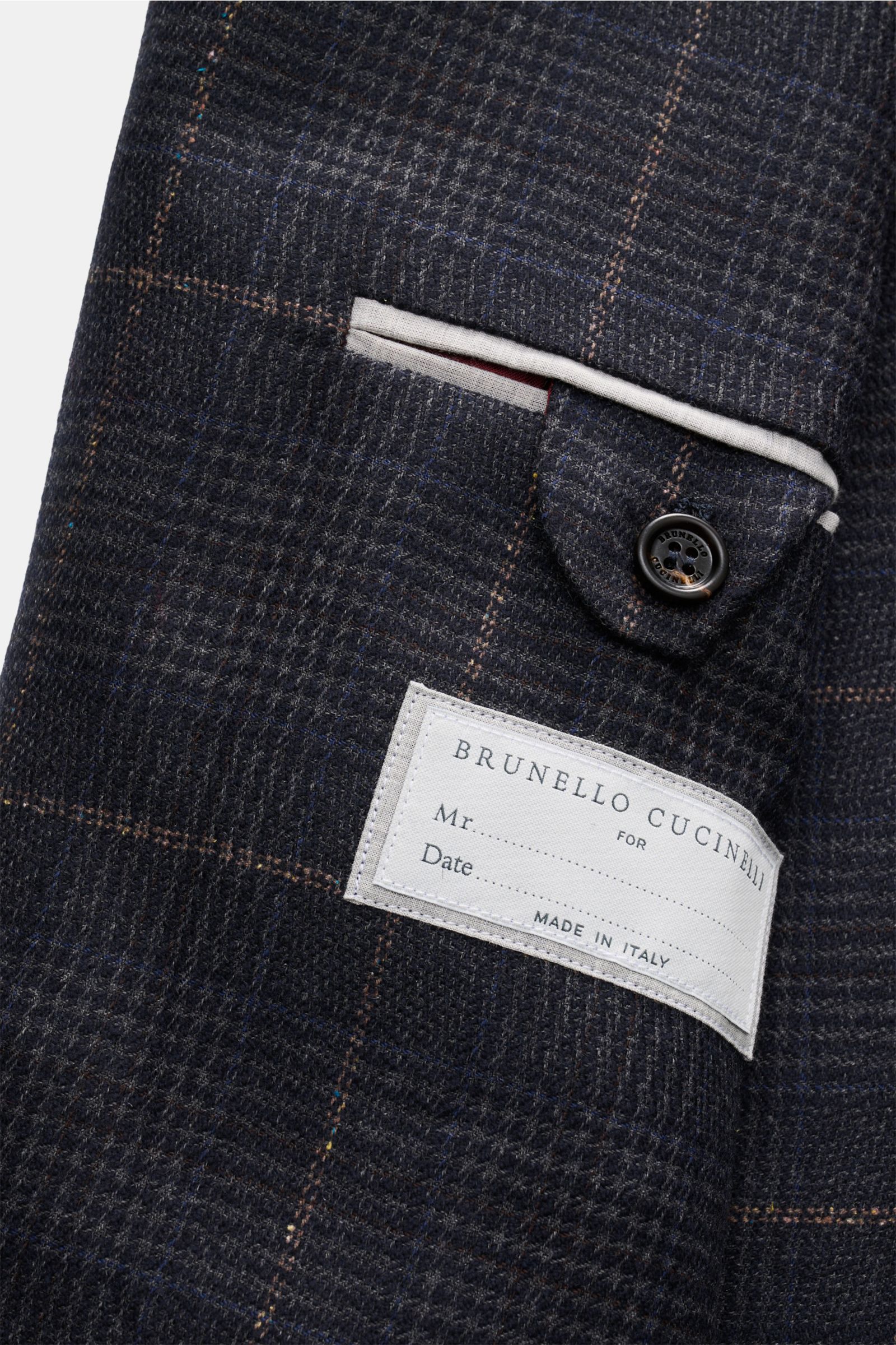 Close-up side view of the Brunello Cucinelli Smart-casual jacket dark grey/navy/light brown checked showing classic glen check pattern, a buttoned flap pocket, and a fabric label stating 'Brunello Cucinelli Made in Italy.' A luxurious classic for sophisti