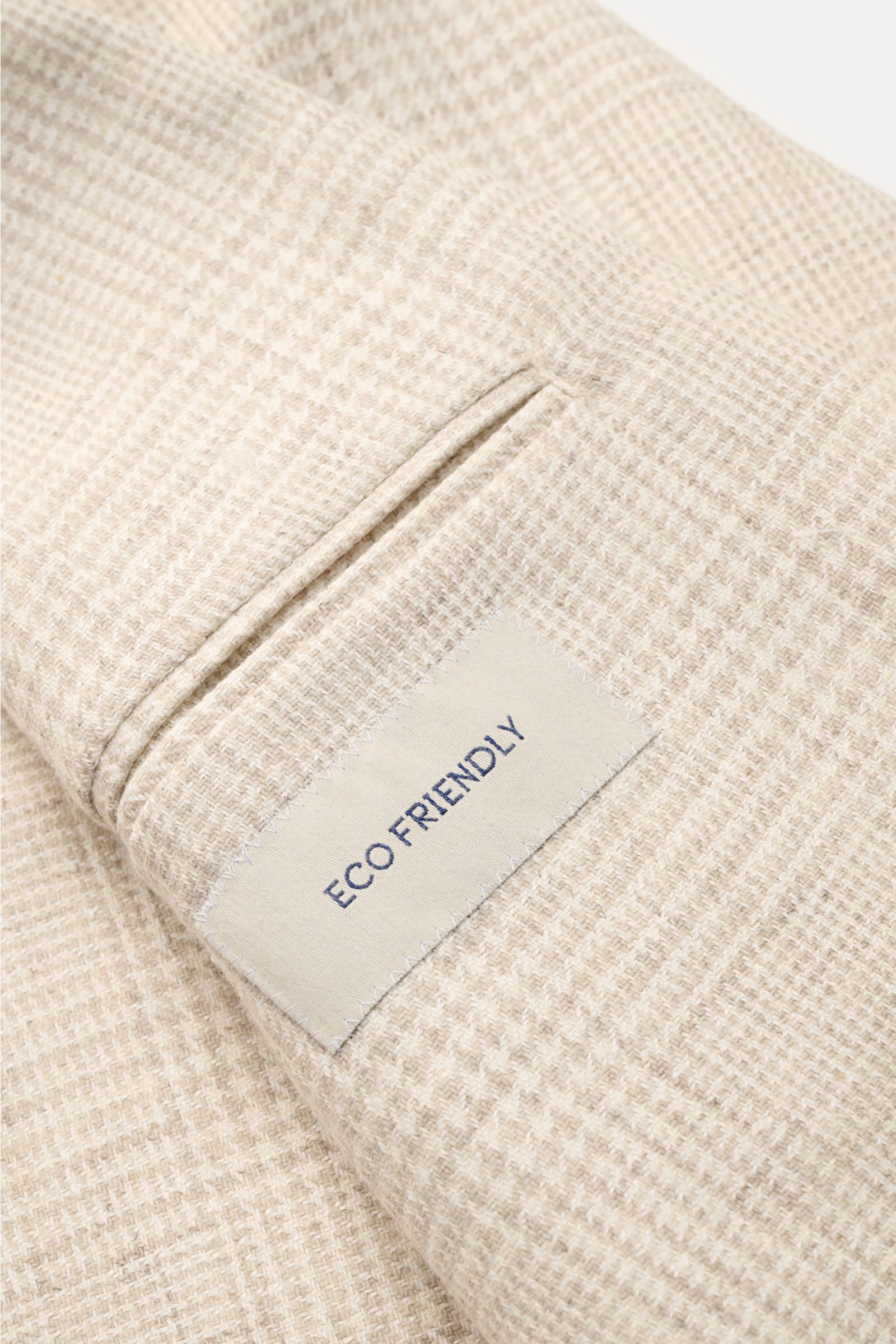 Close-up angled view of the cream/beige checked fabric and pocket detail of the Belvest Smart-casual jacket, featuring an 'ECO FRIENDLY' label. BELVEST has brought together the best in natural materials – wool, linen, silk and cashmere – in this summery s