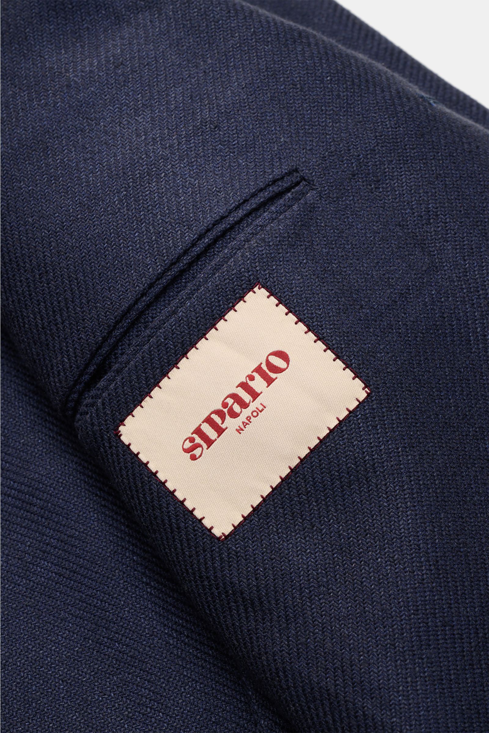 Close-up image of the navy textured fabric and label of the Sipario Sakko 'Ginza' navy, photographed from the sleeve perspective. Leichtigkeit mit Stil: Das Sakko 'Ginza' von SIPARIO setzt auf eine reduzierte, ungefütterte Konstruktion Leinen, Seide un