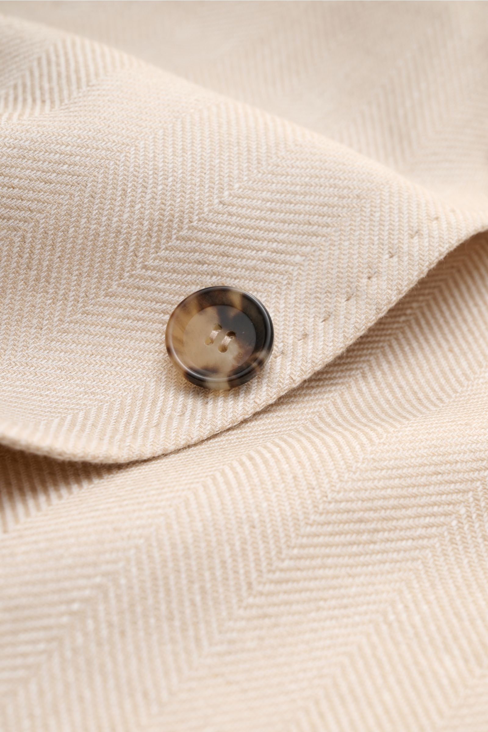 Close-up front view of the Sipario Smart-casual jacket 'Ginza' sand patterned showing lightweight linen and cotton fabric with tonal herringbone and a tortoiseshell button.

Lightweight and stylish: The smart-casual jacket 'Ginza' by SIPARIO features a