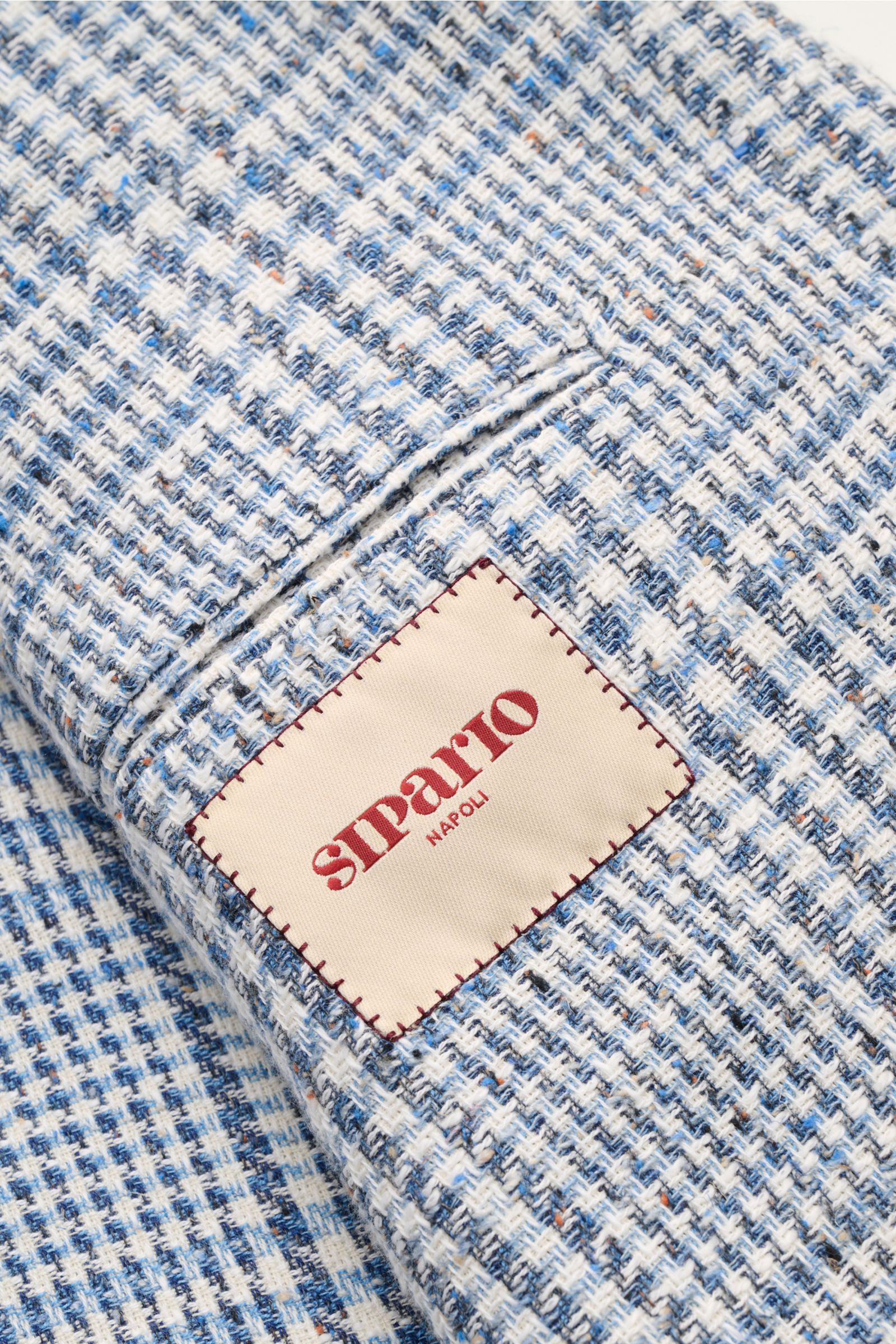 Alt tag (125 characters max): Close-up of the fabric and label of Sipario Smart-casual jacket 'Ginza' grey-blue/off-white checked from a top view.

Description: Structure with style: The smart-casual jacket 'Ginza' by SIPARIO in lightweight cotton Pana