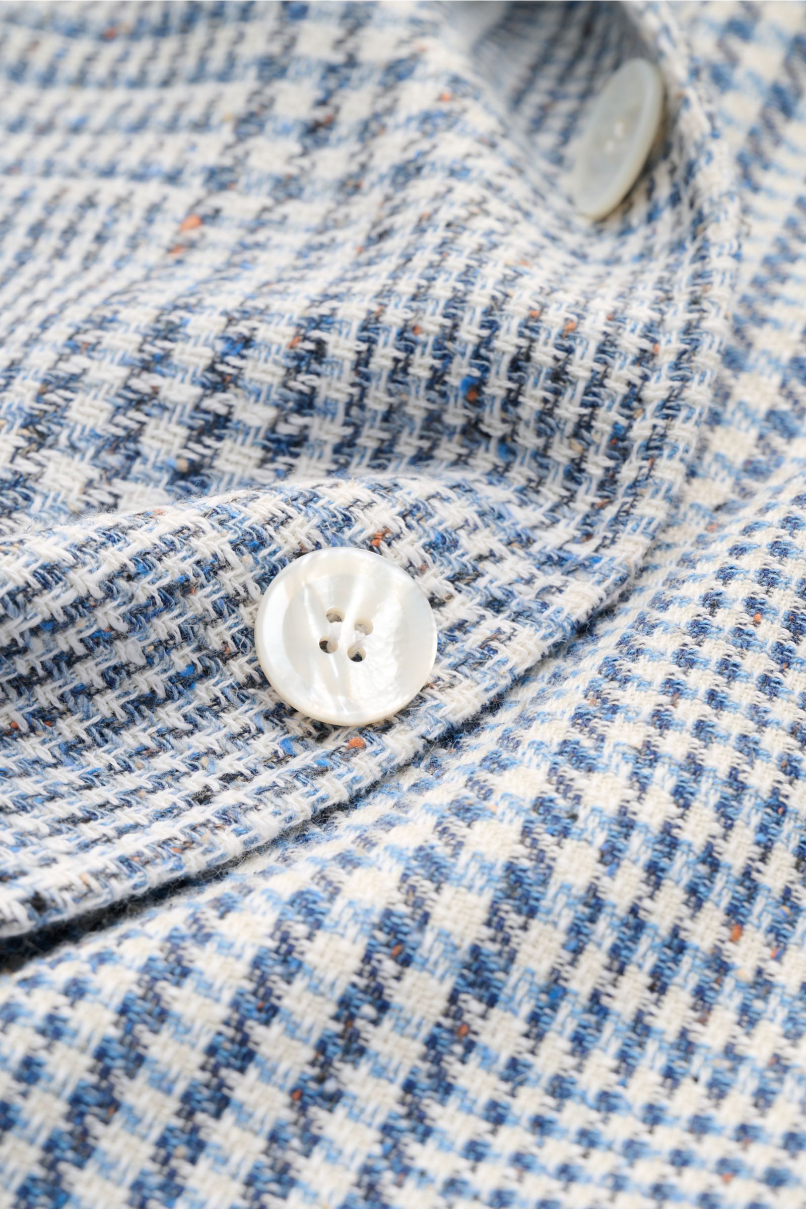Close-up front detail of Sipario Smart-casual jacket 'Ginza' grey-blue/off-white checked in lightweight cotton Panama with pearl buttons.

Description: Structure with style: The smart-casual jacket 'Ginza' by SIPARIO in lightweight cotton Panama is a t