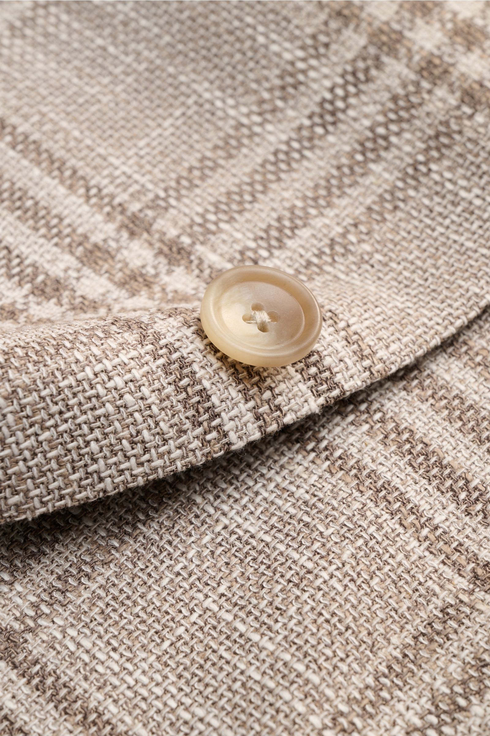 Close-up of the button and textured fabric of the Tagliatore Smart-casual jacket 'Monte Carlo' beige/taupe checked, showcasing the unconstructed finish in a fine blend of virgin wool, cotton, and silk. The elasticated, soft-feel fabric features a slim fit