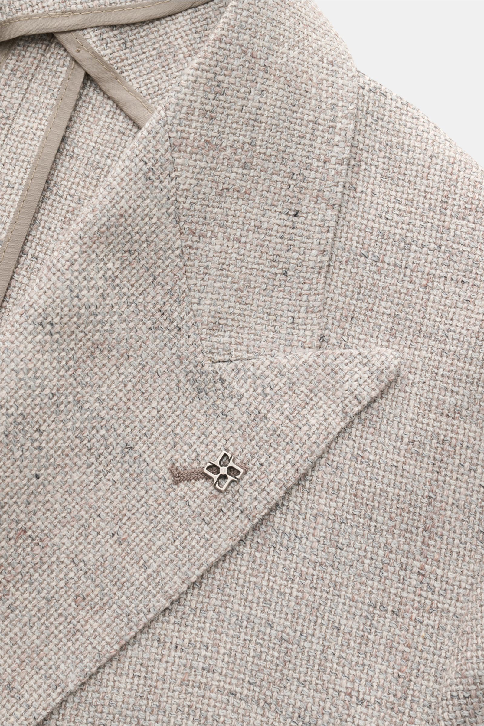 Nahaufnahme des graumelierten Tagliatore Sakkos 'Monte Carlo' in Unconstructed-Verarbeitung, zweireihig, drei Knöpfe, Spitzrevers mit markantem Pin aus Seide, Leinen und Baumwolle im feinen Strukturgewebe.