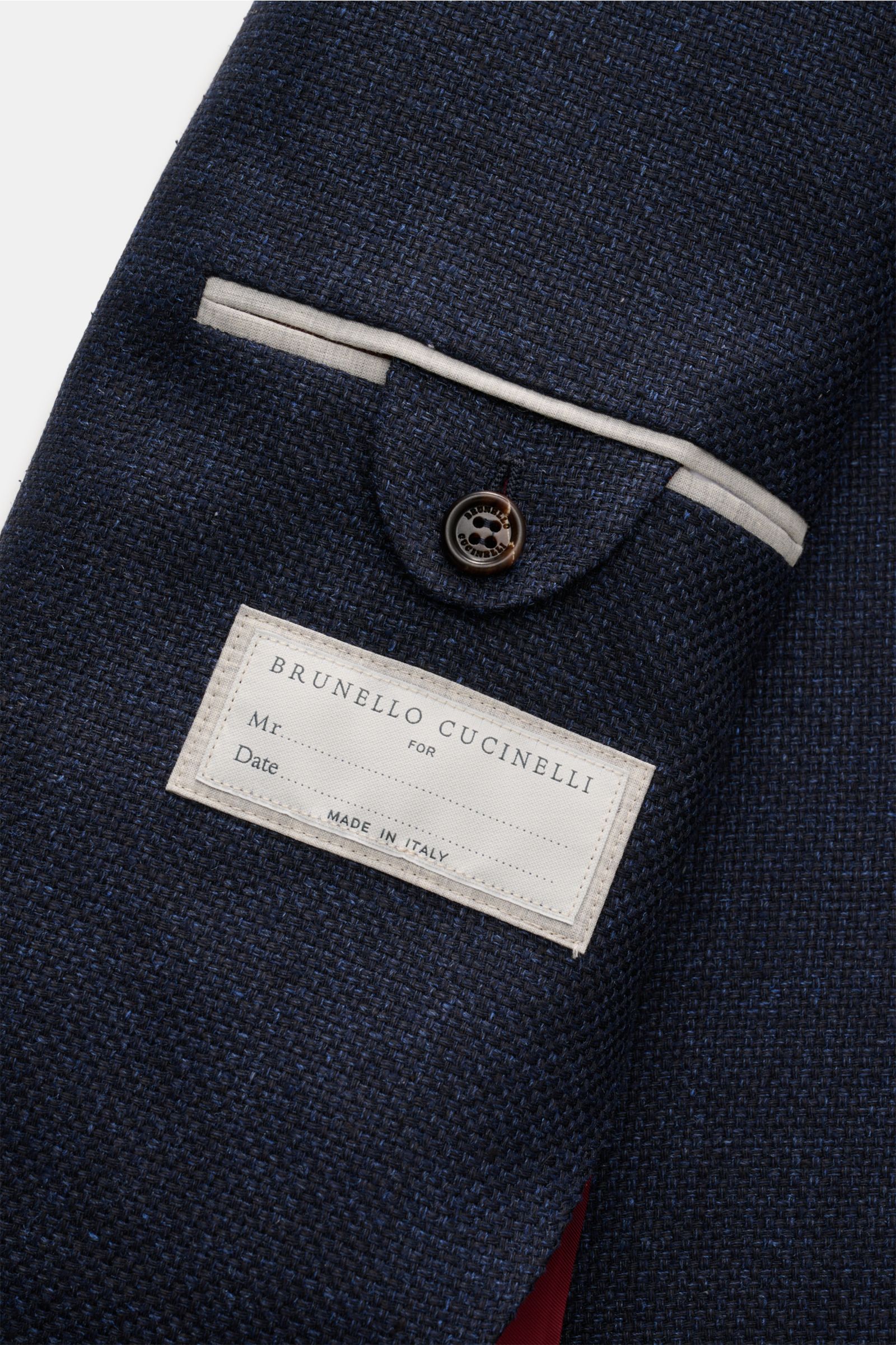 Close-up of the inside pocket of the Brunello Cucinelli Sakko navy meliert, showing the melierte navy fabric with a mix of silk, linen, and wool, a button, and the brand label, photographed from an angled top-down perspective. Leicht, edel und mit unverwe