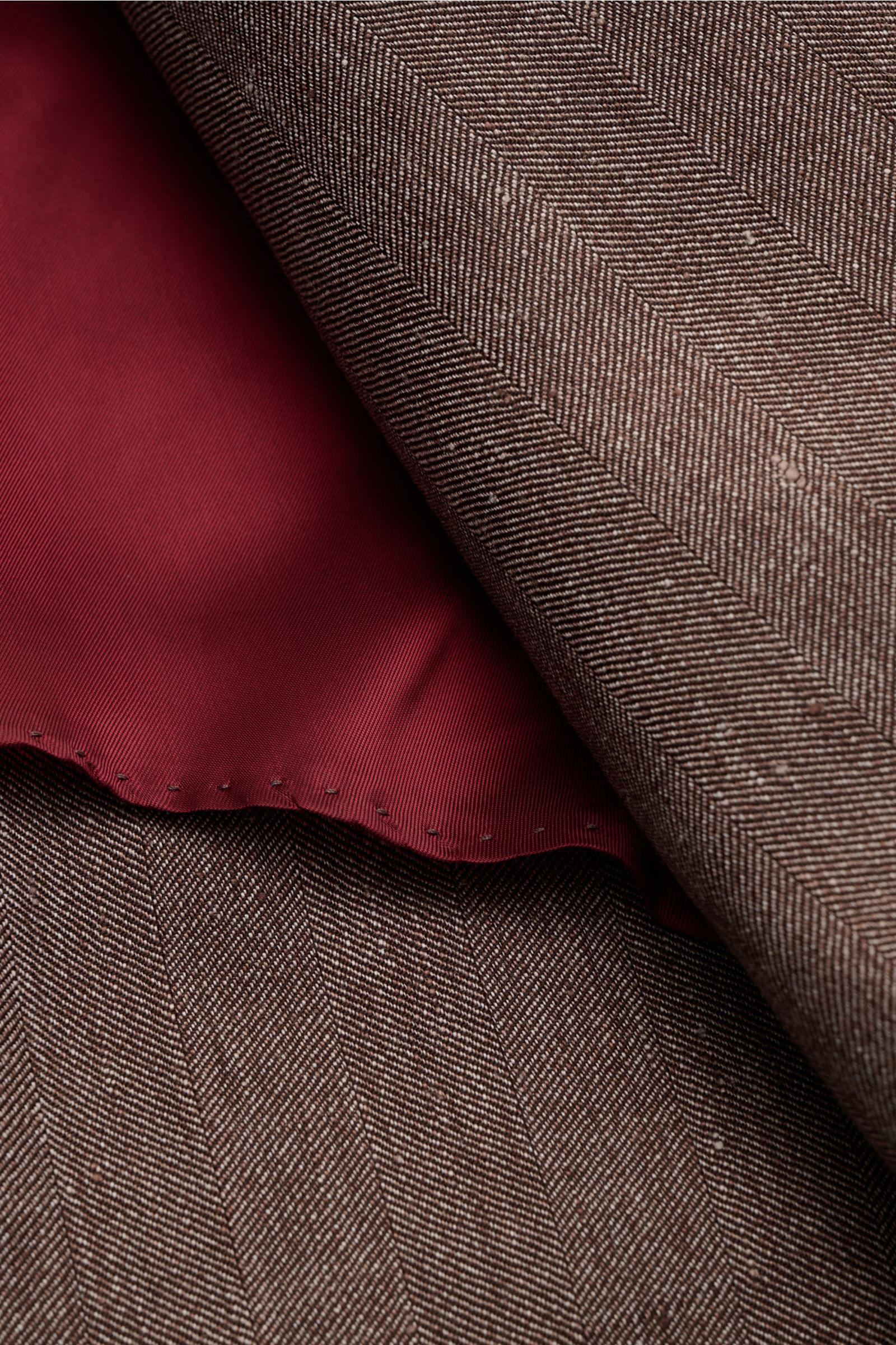 Close-up from above of the Brunello Cucinelli Sakko graubraun meliert showing soft linen-wool fabric with tonal herringbone and red unfinished sleeve lining.