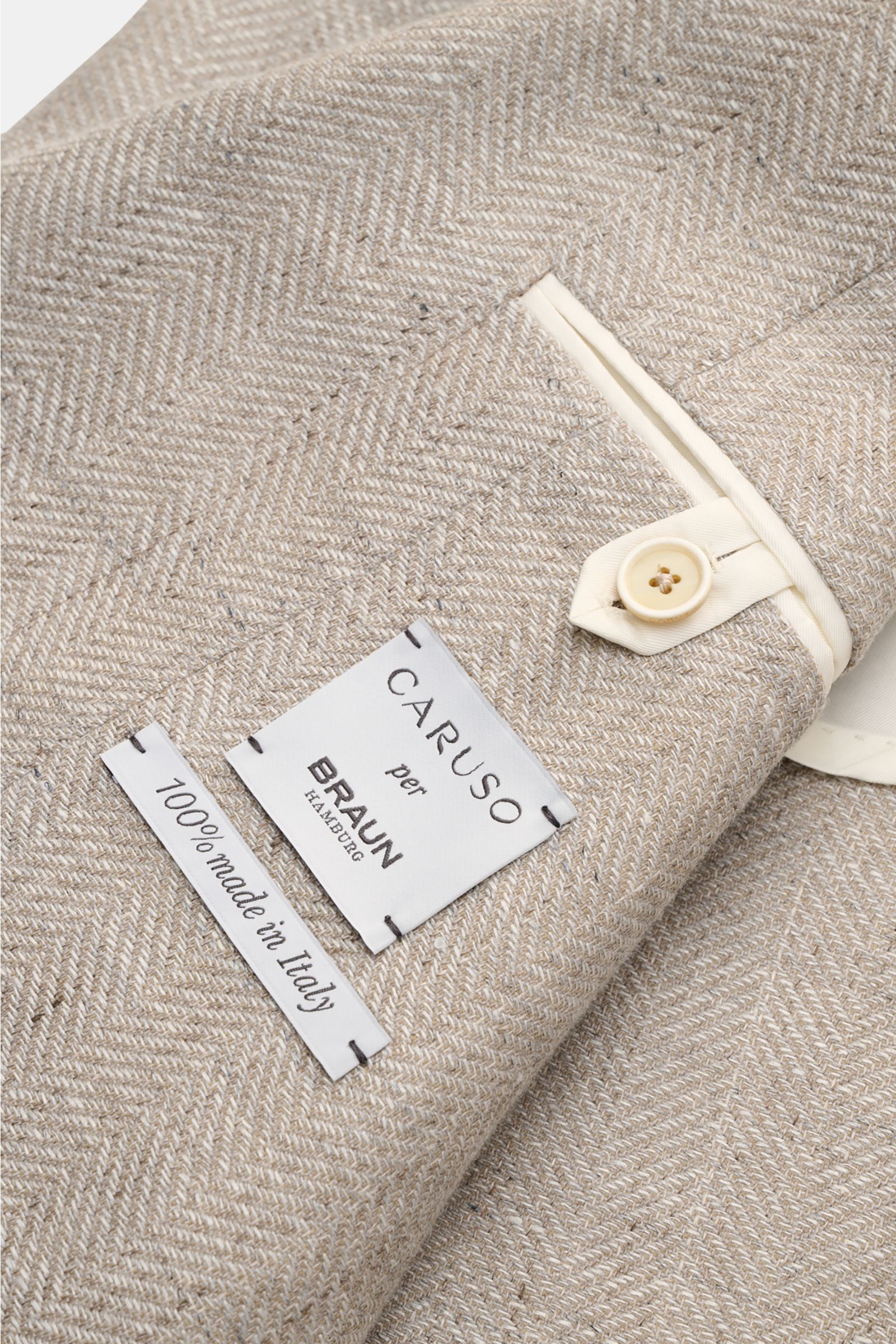 Close-up view of the Caruso smart-casual jacket 'Aida' beige mottled, showing fabric texture, button, and label. 

In the smart-casual jacket 'Aida', CARUSO combines smart style with fabric in the natural materials linen and wool – and the herringbone 
