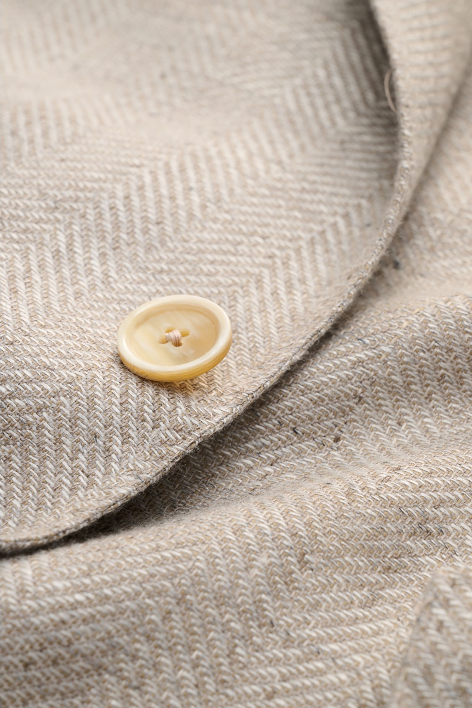 Close-up front detail of Caruso Smart-casual jacket 'Aida' beige mottled showing herringbone texture and button on linen-wool fabric. 

In the smart-casual jacket 'Aida', CARUSO combines smart style with fabric in the natural materials linen and wool –