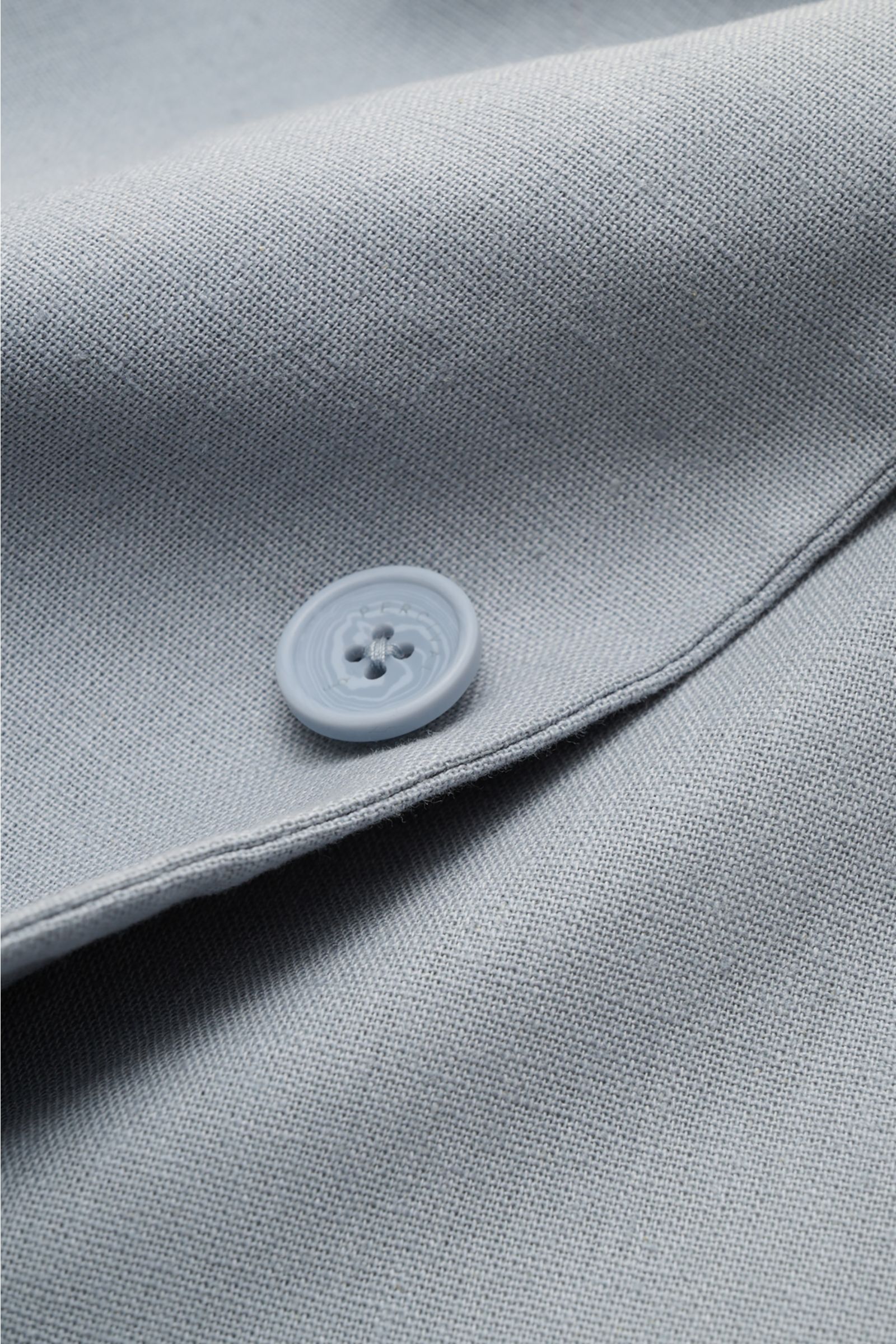 Close-up image of the fabric and button detail of the Percival Smart-casual jacket 'Tailored Linen' smoky blue, photographed from a top-down perspective. Combines texture and everyday suitability: This versatile smart-casual jacket by PERCIVAL combines ma