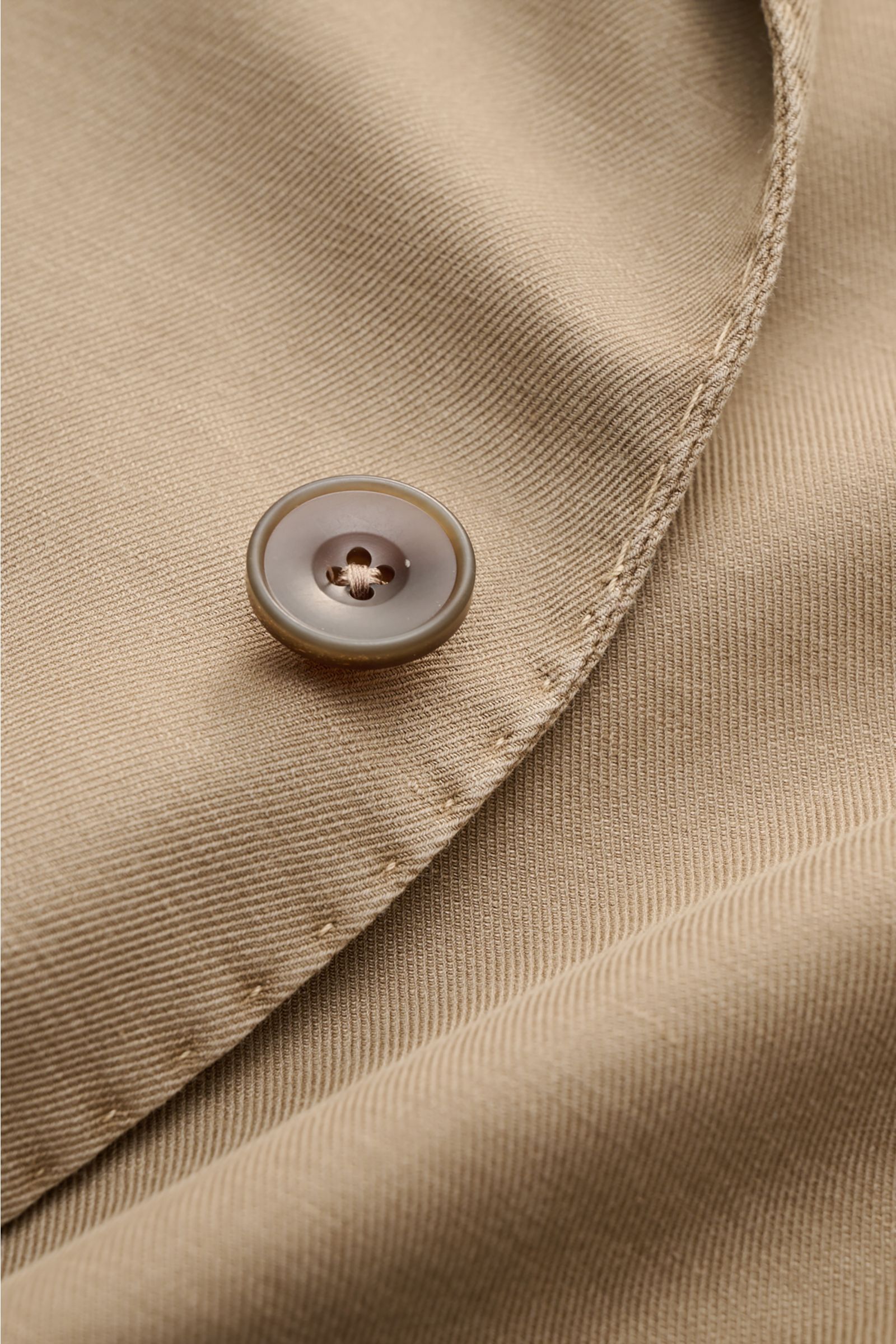 Nahaufnahme des taupefarbenen Santaniello Sakkos mit Fokus auf den Knopf und die feine Baumwoll-Leinen-Mohair-Struktur, Slim Fit, zwei Knöpfe, fallendes Revers, klassische Brust- und Hüfttaschen, Kissing Buttons, Seitenschlitze, Unconstructed Design, drei