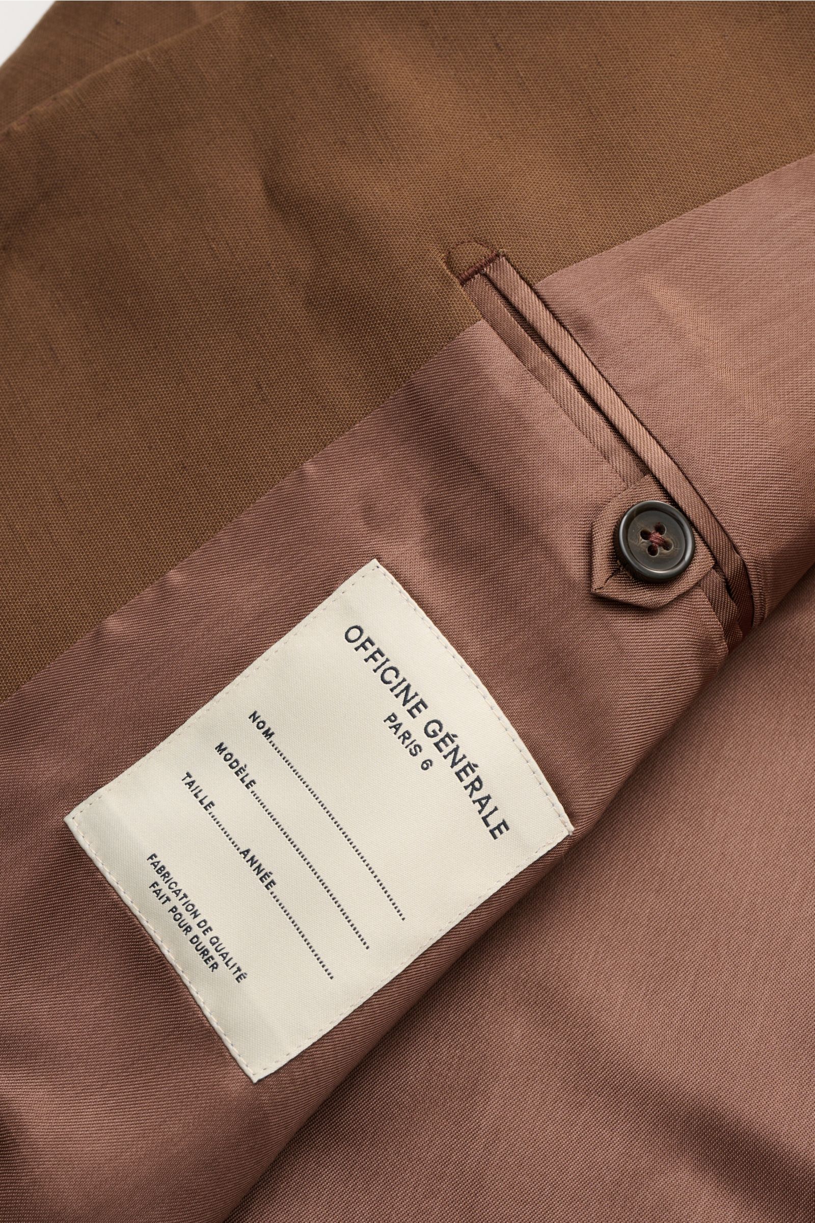Nahaufnahme des Innenfutters vom Officine Générale Sakko 'Michel' braun, mit glattem Griff, Knopf und Label, seitliche Perspektive.