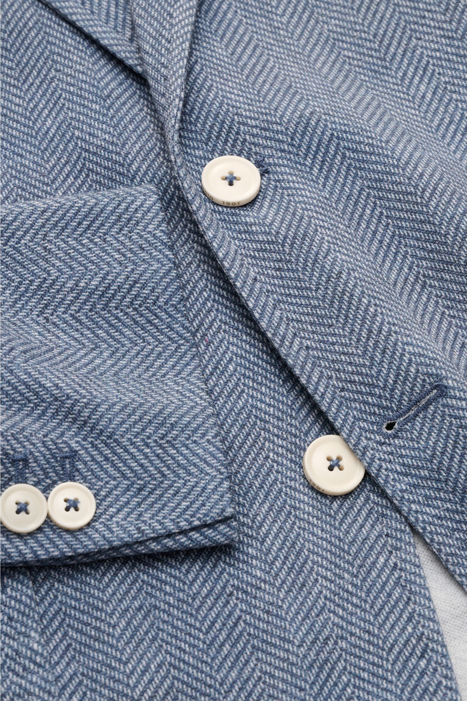 Nahaufnahme des Circolo 1901 Jersey-Sakkos rauchblau/weiß gemustert mit Fischgrat-Muster, Knöpfen und Brusttasche, Perspektive von oben.