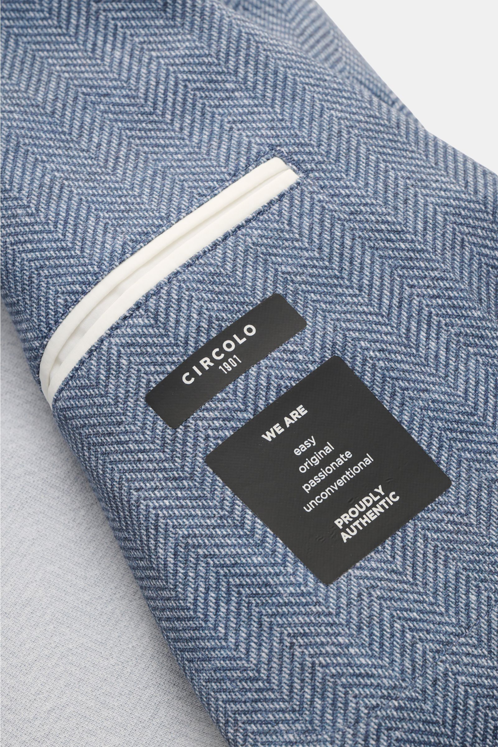 Nahaufnahme des Circolo 1901 Jersey-Sakkos rauchblau/weiß gemustert mit Fischgrat-Muster, weichem Jersey, Slim Fit und Unconstructed-Design, sichtbare Innentasche mit weißem Besatz, fotografiert von oben.