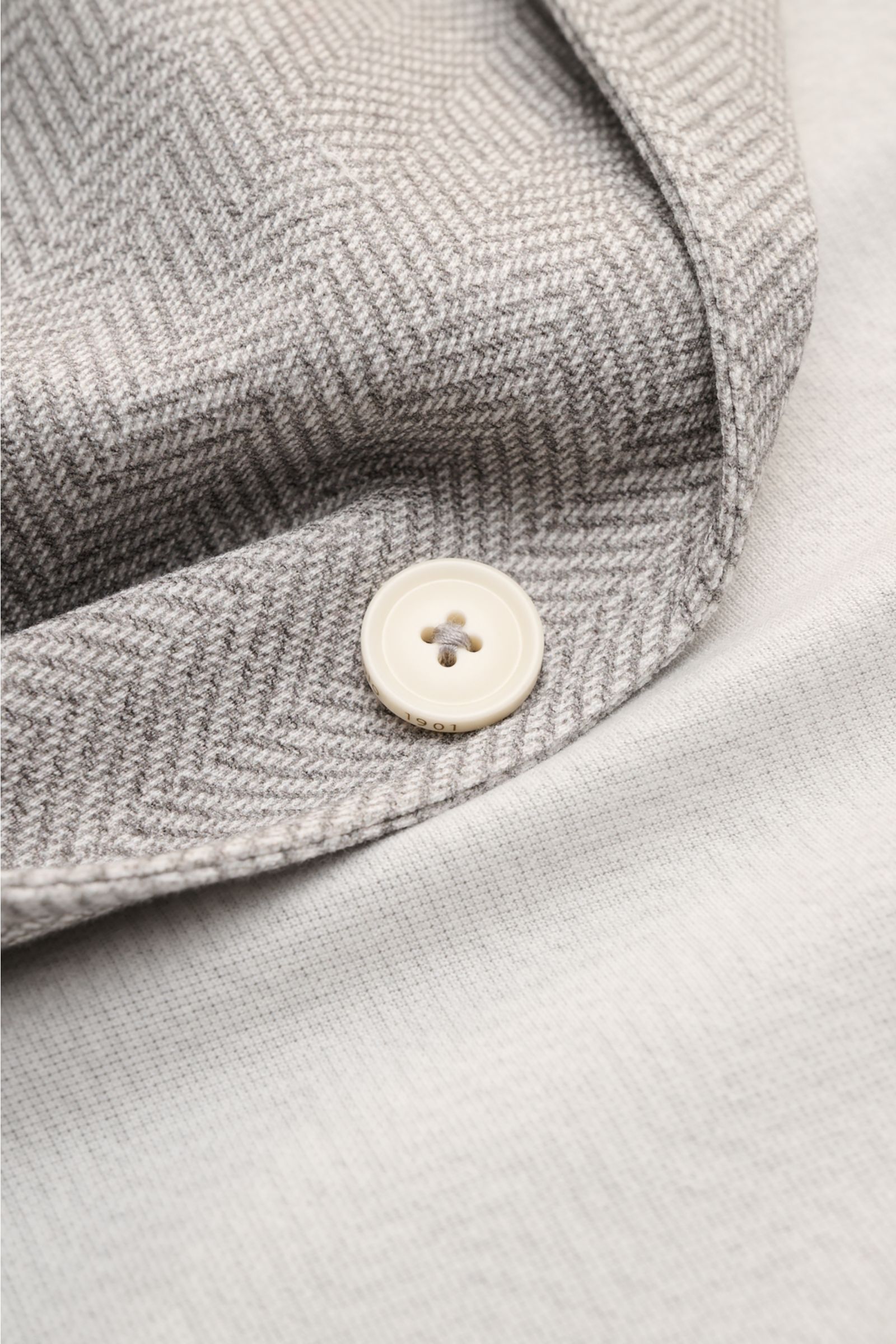 Nahaufnahme von Kragen und Knopf des Circolo 1901 Jersey-Sakko grau/offwhite gemustert mit Fischgrat-Muster, weichem Jersey aus elastischer Baumwolle, Slim Fit und Unconstructed-Design.