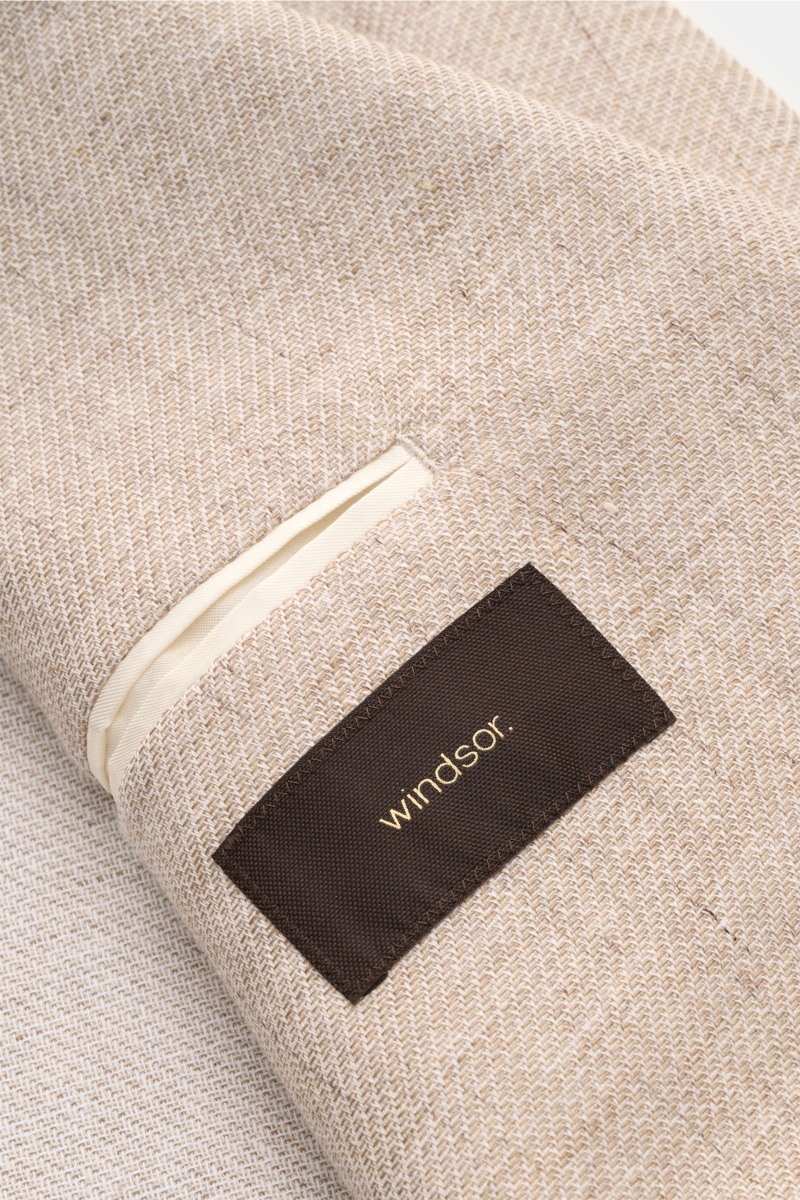 Close-up top view of the Windsor Smart-casual jacket 'Giorno' beige mottled fabric showing a cream trim pocket and black label with gold Windsor text. 

Stylish and uncomplicated: With the lightweight, unconstructed 'Giorno' smart-casual jacket by 