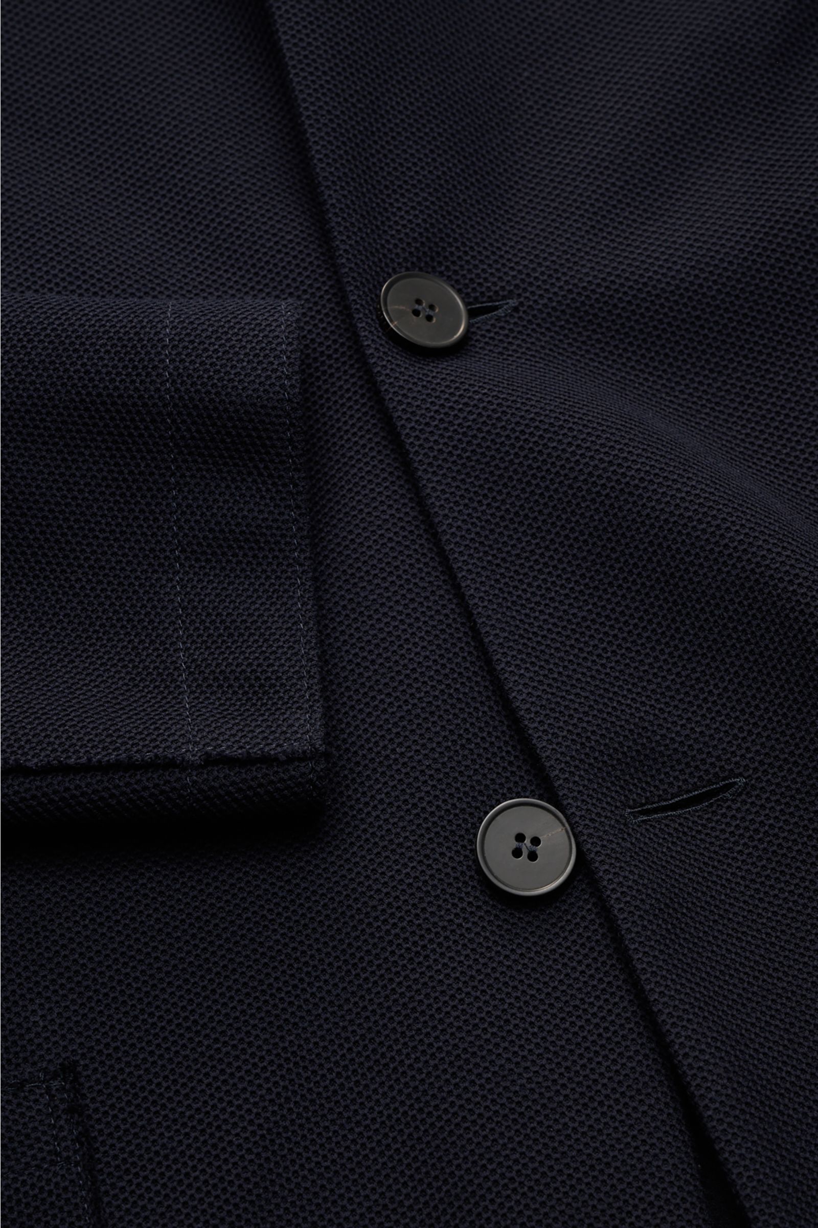 Harris Wharf London Knit blazer navy shown in close-up from a top-down angle, featuring pure cotton piqué, four buttons, patch hip pockets, and open edge finish, slim fit with a slim standing collar, unlined with two inside pockets. HARRIS WHARF LONDON