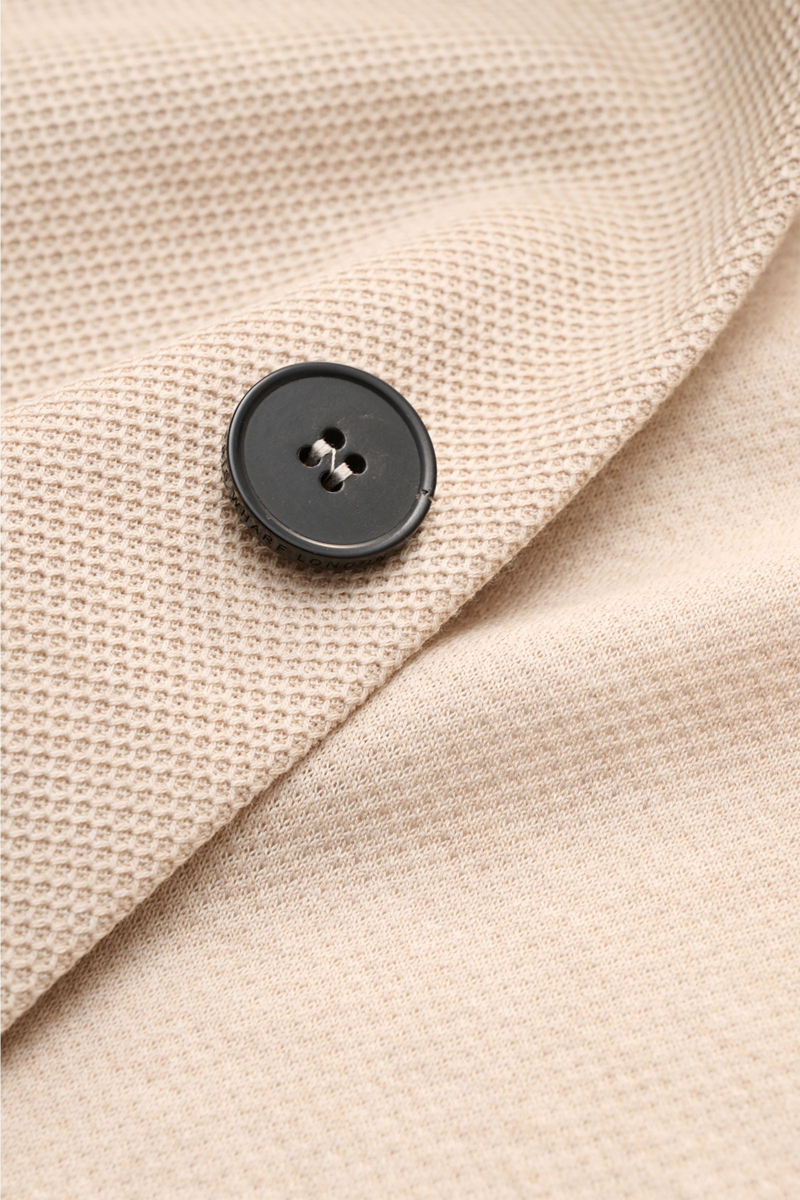 Close-up front view of the Harris Wharf London Knit blazer beige showing its textured pure piqué cotton fabric and a black four-hole button. 

HARRIS WHARF LONDON has chosen a high-quality cloth from Loro Piana for this relaxed knit blazer. Pure cotton