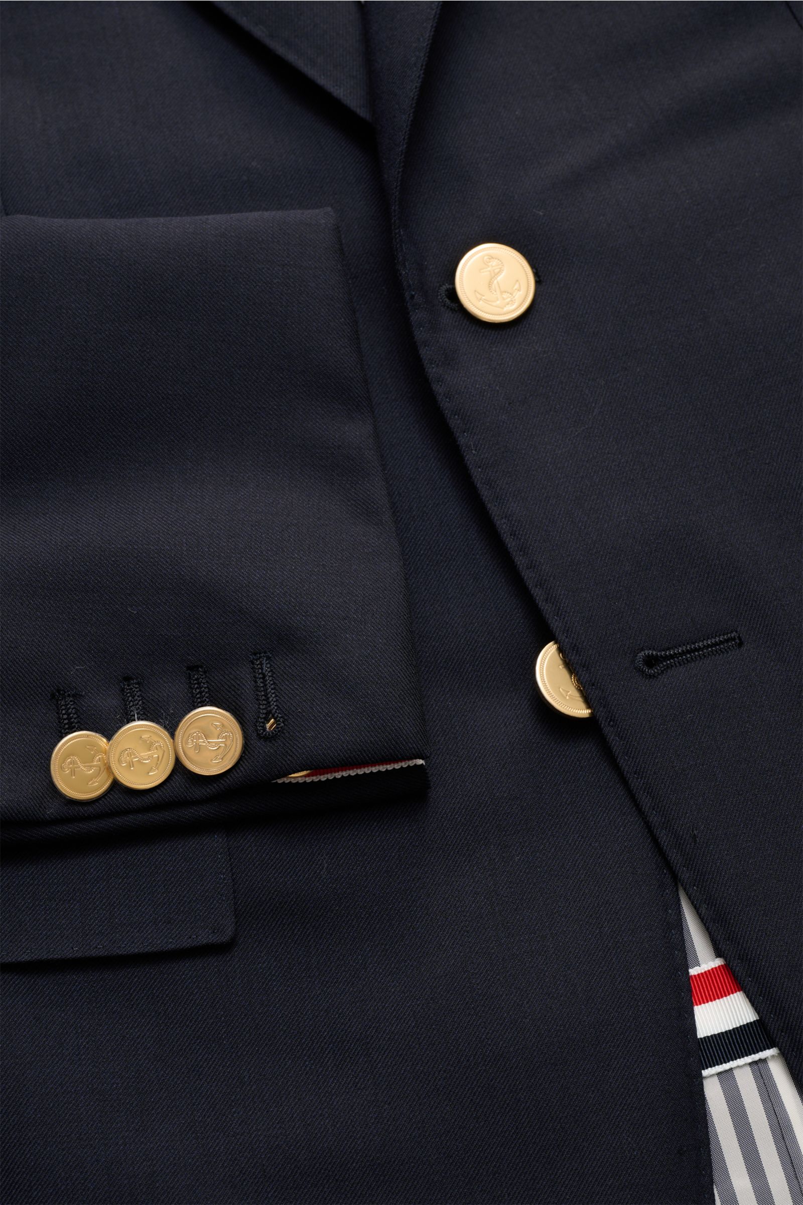 Nahaufnahme von Thom Browne Sakko navy aus reiner Wolle mit goldfarbenen Kissing Buttons, fallendem Revers und Ripsband-Tricolore, Slim Fit.