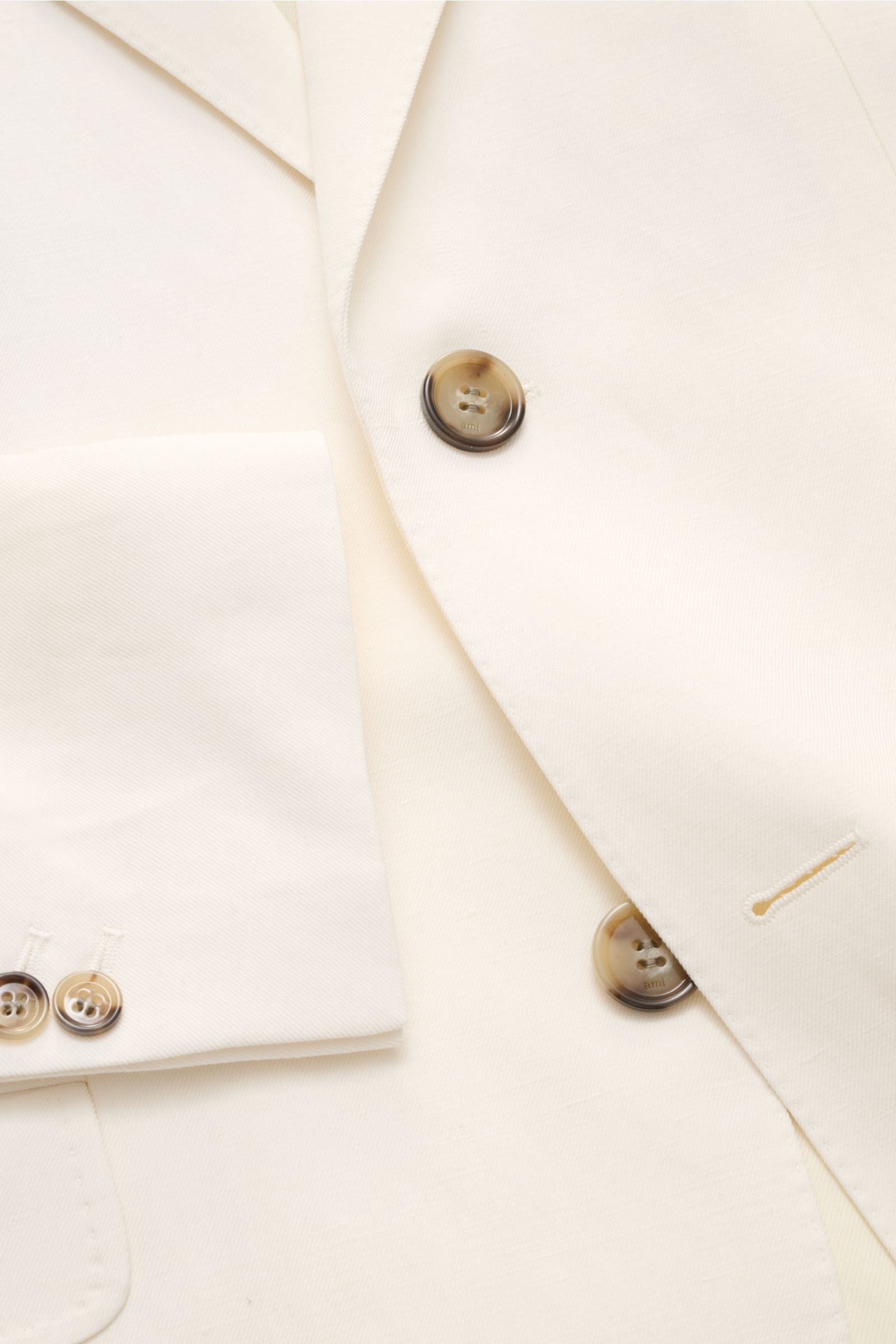 Nahaufnahme des Ami Paris Sakko creme von vorne oben, zeigt Slim Fit, fallendes Revers, zwei Knöpfe, Brust- und Hüfttaschen, Ärmel mit Knöpfen.