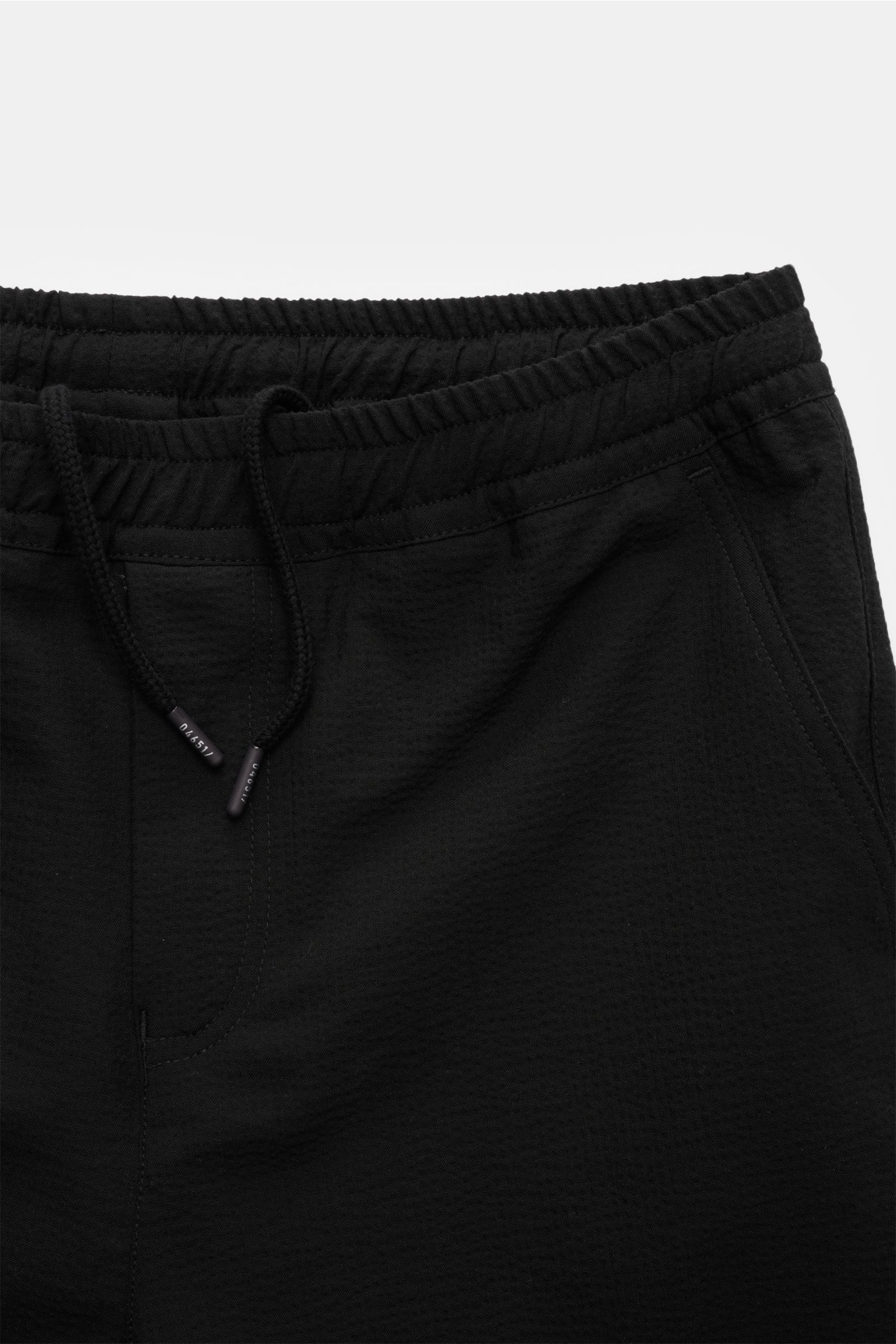 Close-up front view of the black 04651/ A trip in a bag Seersucker-Hose schwarz, made of seersucker wool and microfiber, showing tapered fit, regular thigh width, shortened leg length, elastic waistband with internal drawstring, French pockets, patch back