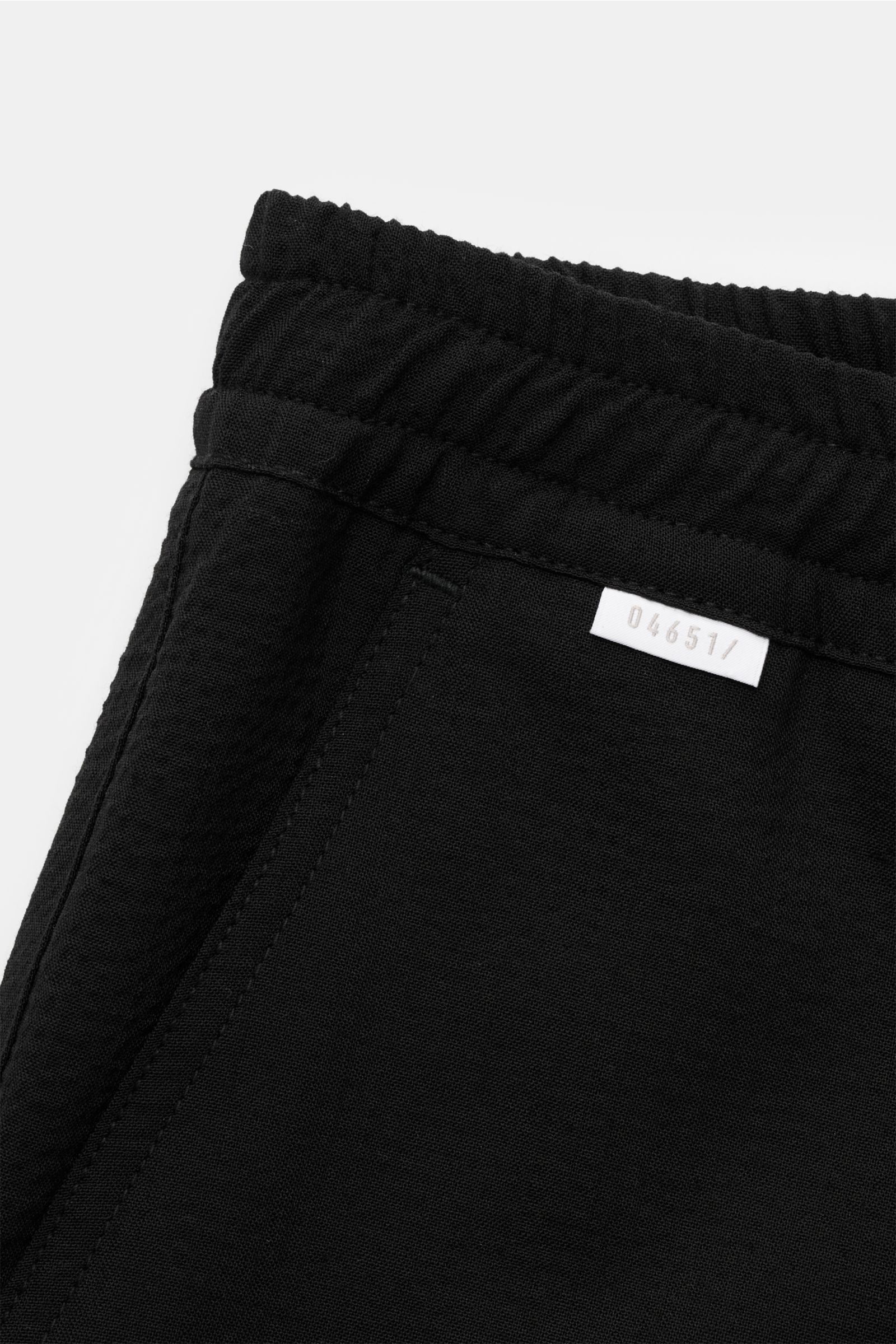 Close-up front-side view of black '04651/ A trip in a bag Seersucker-Hose schwarz' featuring seersucker wool and microfiber, elastic waistband with inner drawstring, tapered fit, regular thigh width, shortened leg length, French pockets, patch back pocket