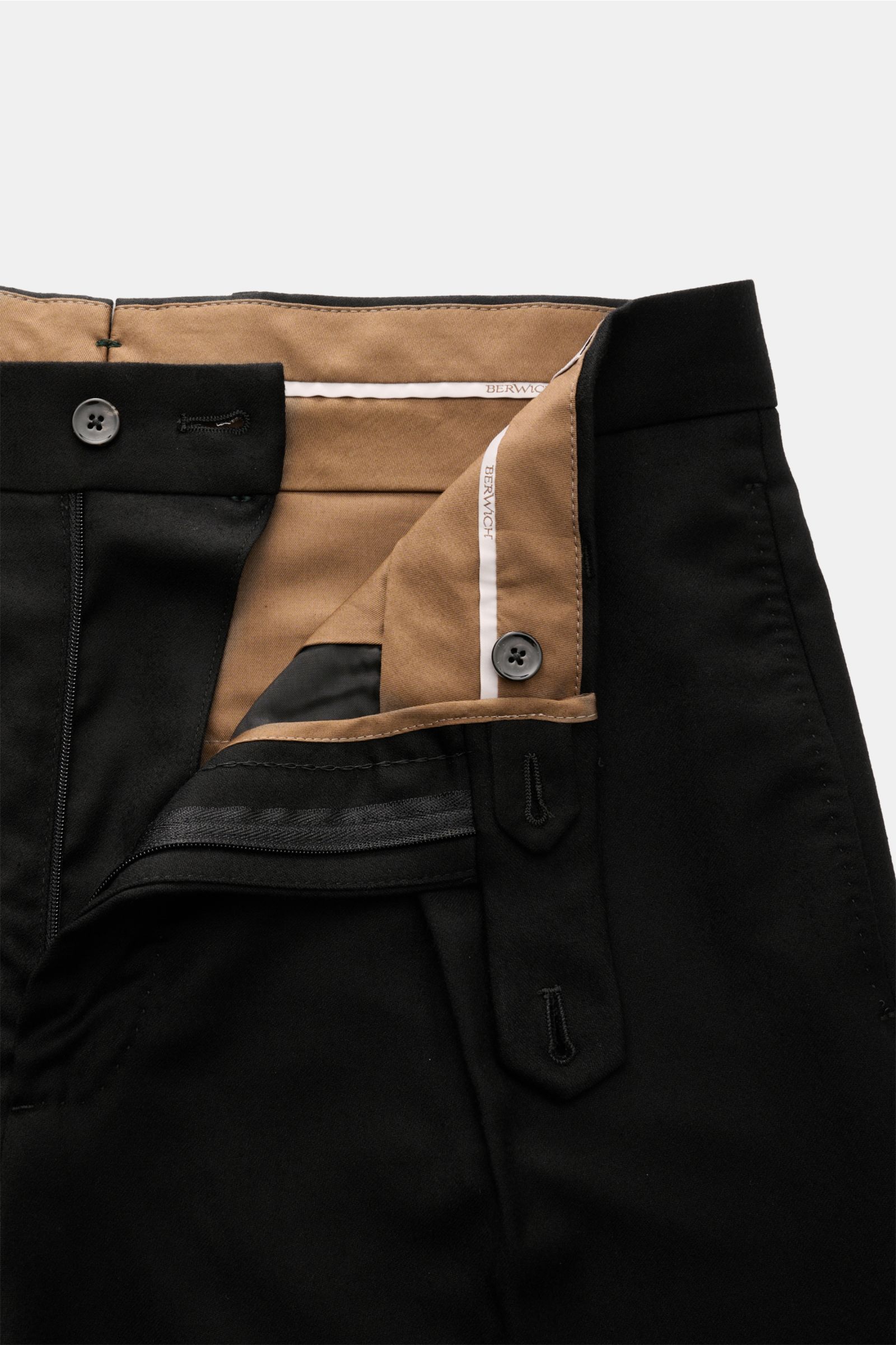 Close-up from above of Berwich Wool trousers 'Chiaia' black showing zip, waist buttons, extended buttoned tab, and inner beige lining; pure virgin wool, soft feel, tapered fit with regular thigh width, ankle length, simple pleats, side seam pockets, hip p
