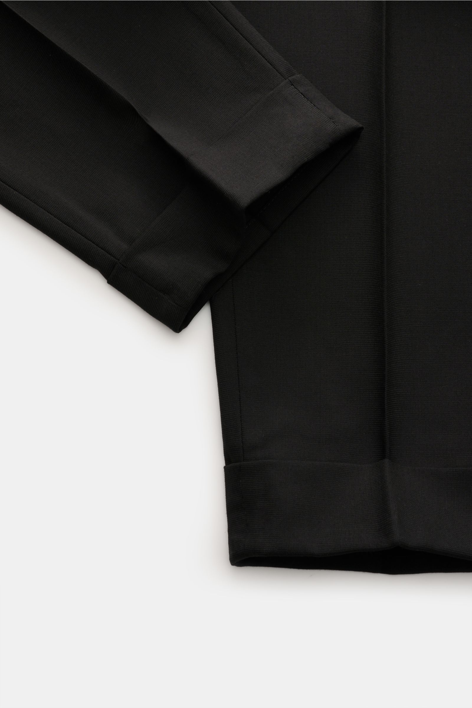 PT Torino Jersey trousers 'Carrot Fit' black shown from a close-up top-down view focusing on the ankle length with fixed hem turn-up and tapered cut. With their short cut, stylish pleats and elongated buttoned tab, the jersey trousers 'Carrot Fit' by PT T