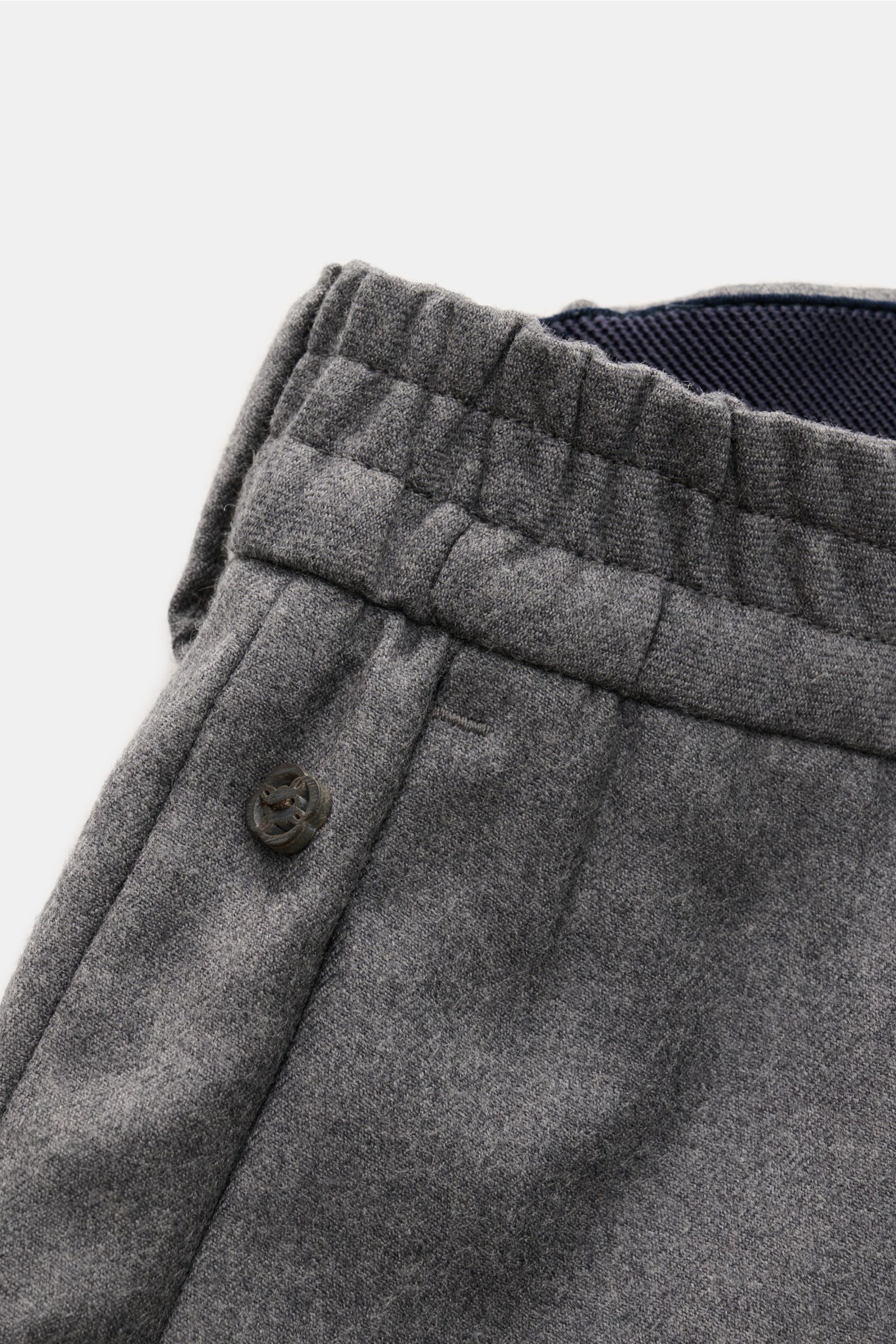 Nahaufnahme von Bund und Oberschenkel der dunkelgrau melierten GTA Woll-Jogpants 'Dennis' aus reiner Schurwolle mit elastischem Bund, Knopf und feinem Logo.