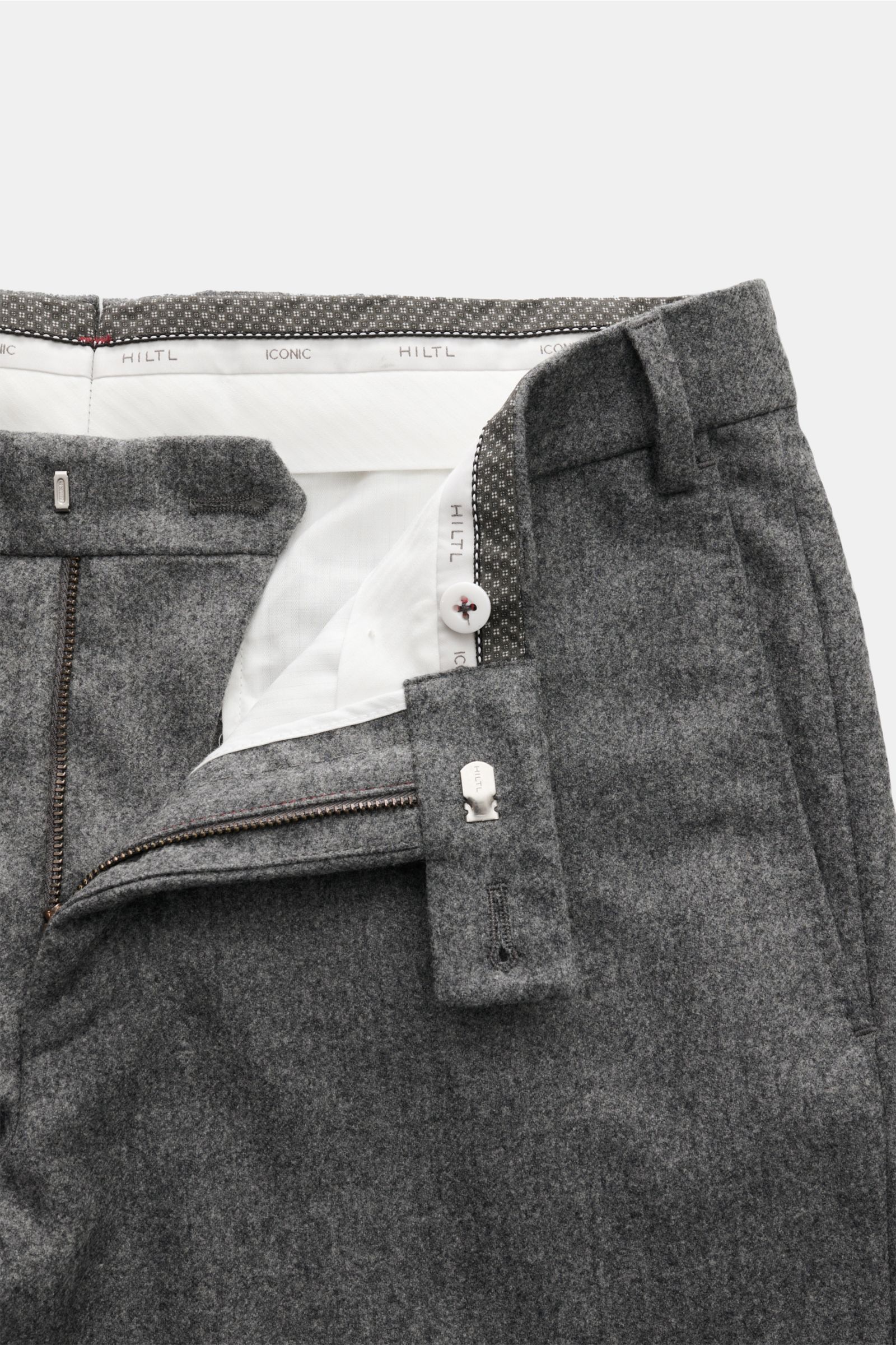 Nahaufnahme der geöffneten Hiltl Wollhose 'Piacenza' grau meliert mit Reißverschluss, Bundknopf, französischen Taschen und Regular Fit, fotografiert von oben.
