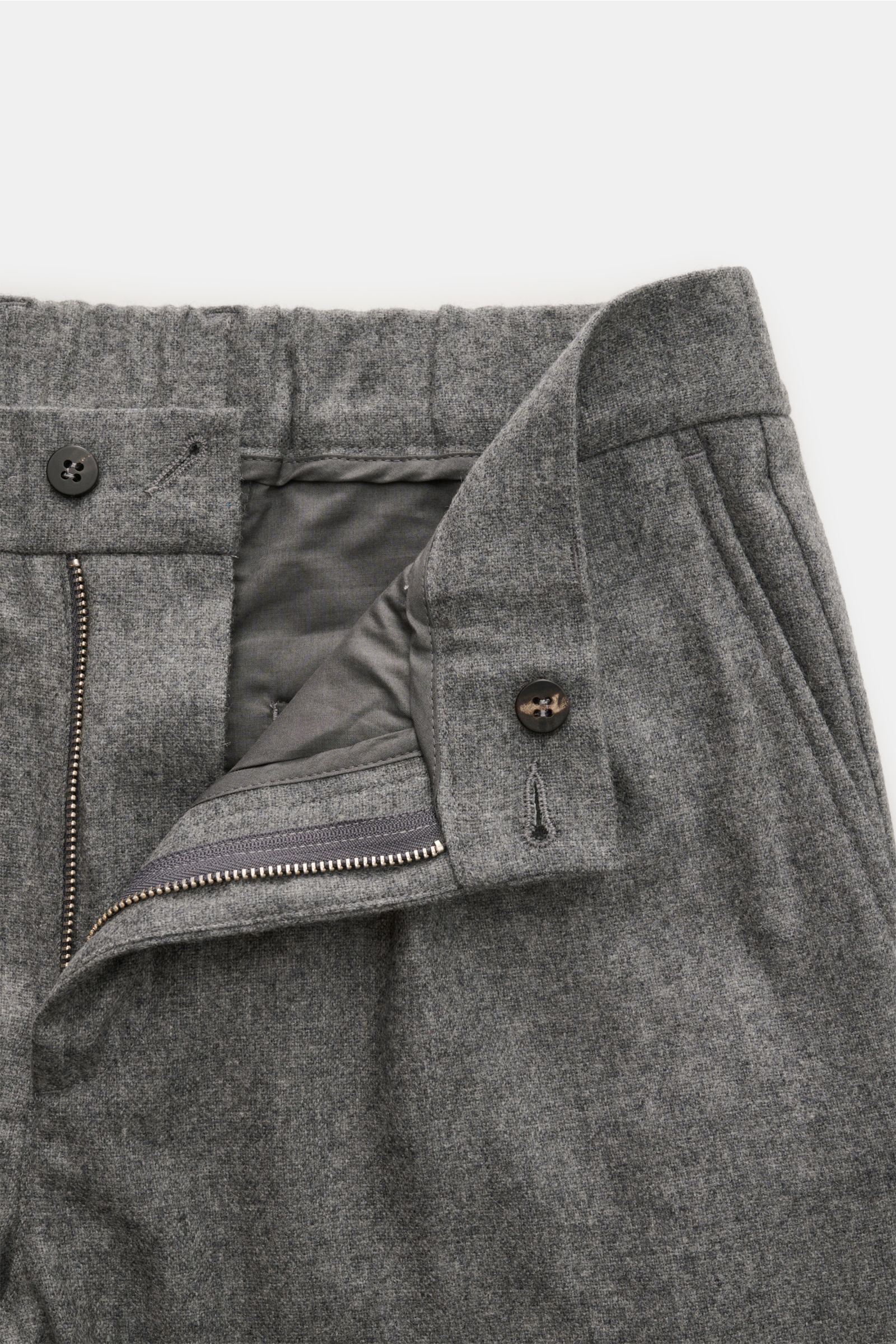 Gray close-up of the open waistband of 04651/ A trip in a bag Hose grau meliert showing a wool-microfiber blend with button, zipper, and soft fabric, photographed from above. Stilvoller Allrounder: Die elegante Hose aus der 'Look of the Games' Capsule von