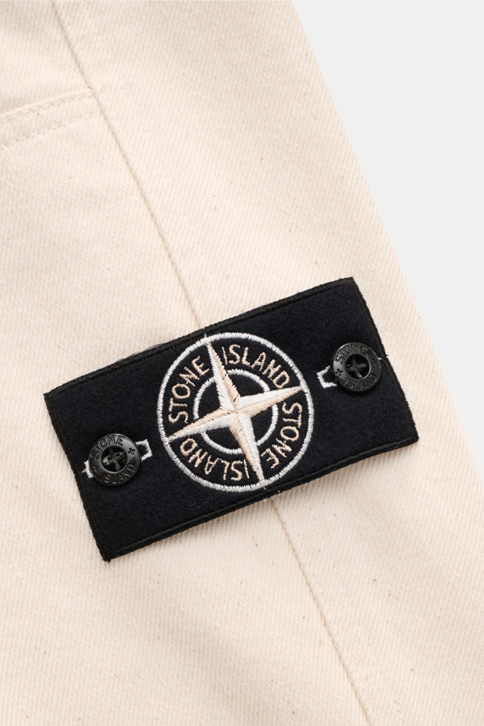 Close-up front view of Stone Island Jogger pants 'Raw Beauty' cream showing distinctive pure cotton twill, robust feel, and signature compass badge.

Description: These robust jogger pants called 'Raw Beauty' by STONE ISLAND are made of distinctive pur