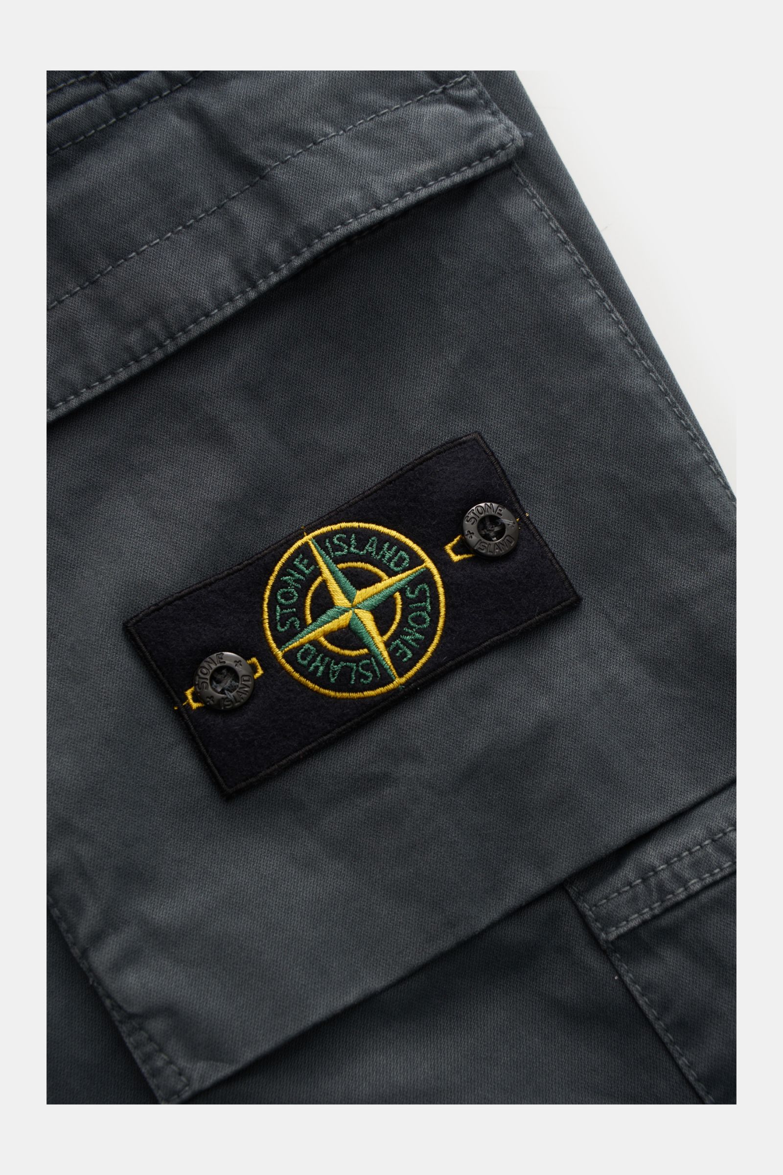 Stone Island Cargo-Jogpants dunkelgrau in Nahaufnahme von oben, zeigt Cargo-Tasche mit typischem Kompass-Badge aus Bio-Baumwolle, elastisch.