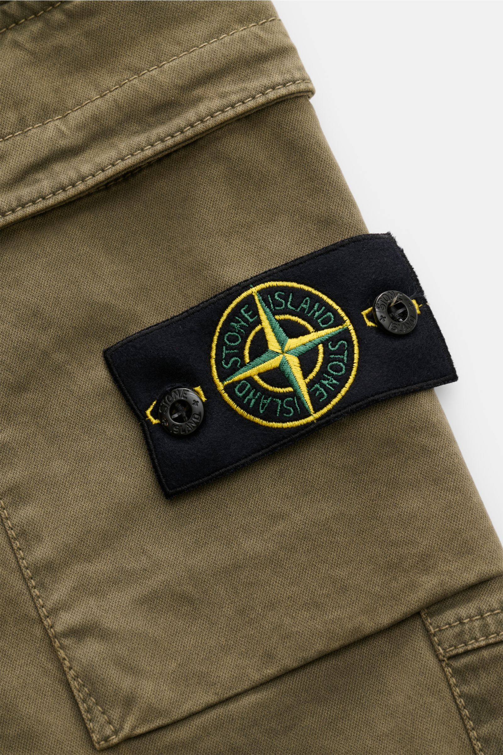 Nahaufnahme aus schräger Perspektive der typischen Stone Island Cargo-Jogpants oliv mit gesticktem Kompass-Badge auf der Cargo-Tasche aus elastischer Bio-Baumwolle.