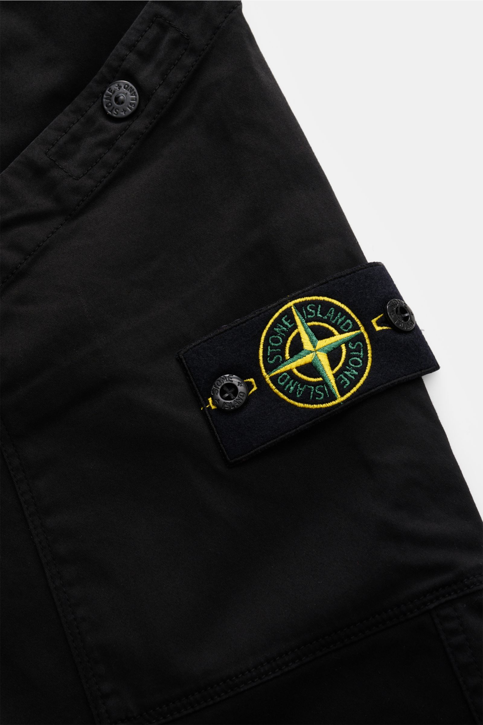 Stone Island Cargohose schwarz, Nahaufnahme der Cargo-Tasche mit Kompass-Badge, Druckknöpfen und Bio-Baumwolle, seitliche Perspektive.
