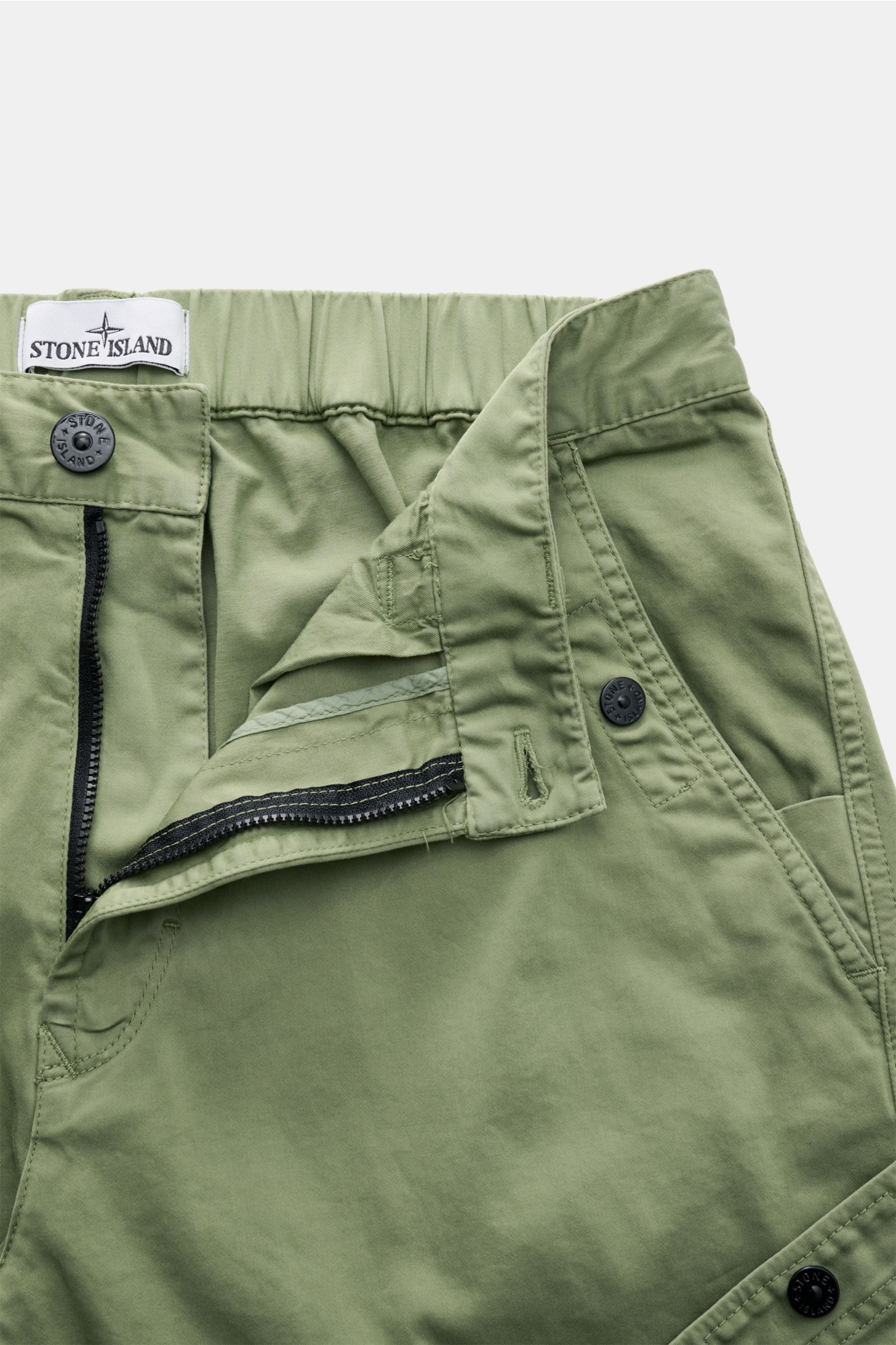 Stone Island Cargohose oliv aus Bio-Baumwolle, teil-elastischer Bund, Reißverschluss, Druckknopftaschen, Kompass-Badge, frontal nah fotografiert.