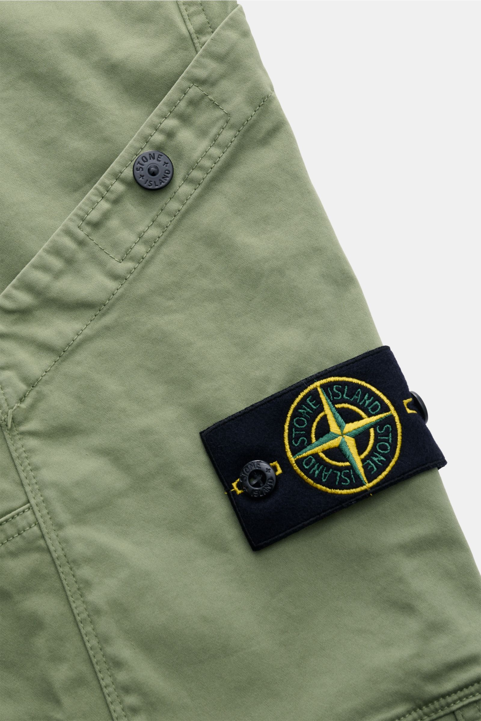 Stone Island Cargohose oliv, Detailansicht der Cargo-Tasche mit Druckknopf und typischem Kompass-Badge aus Bio-Baumwolle.