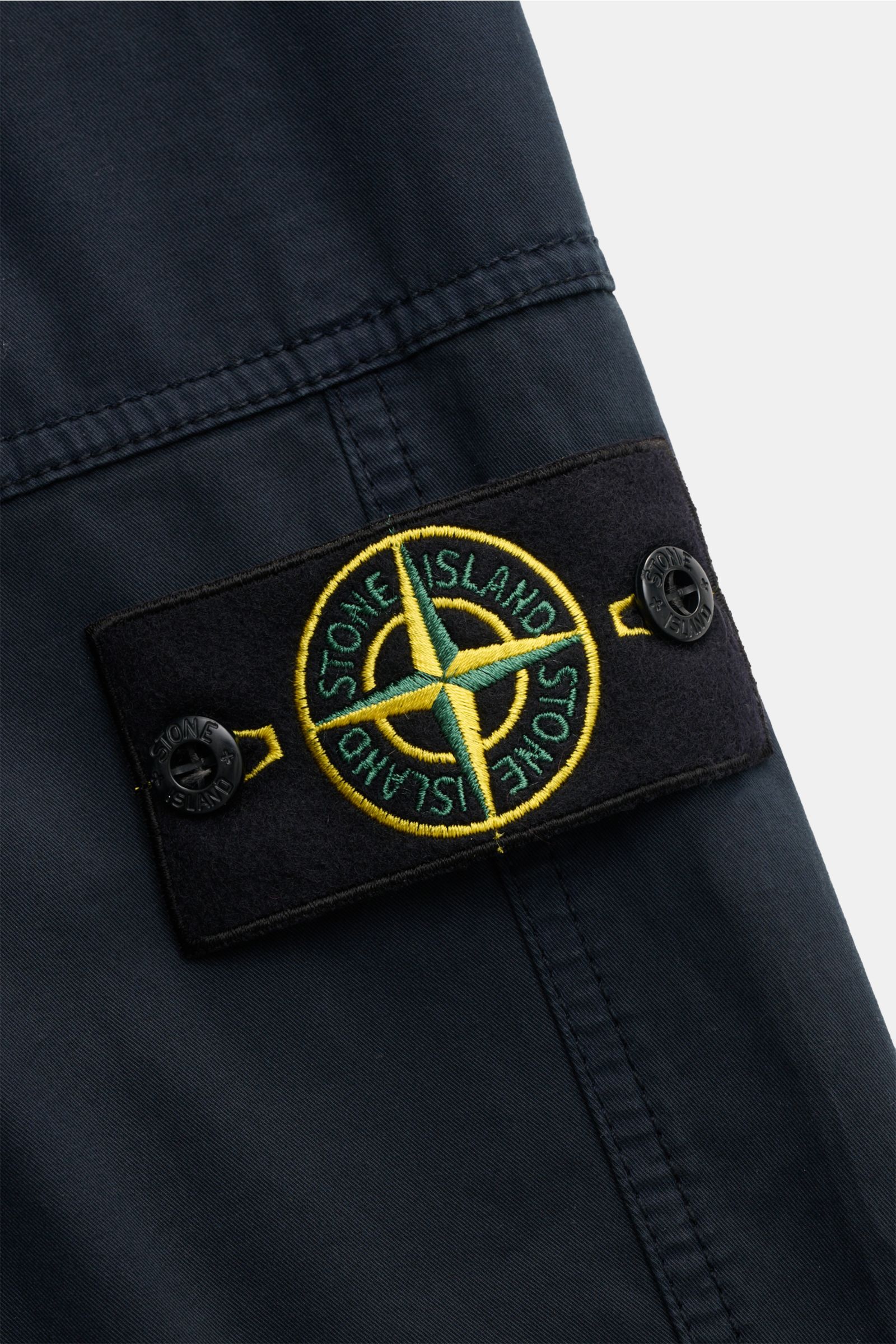 Close-up front view of Stone Island Joggpants navy showing the compass badge on navy lightweight elastic cotton fabric with soft touch, garment dyed, regular fit, elastic waistband with drawstring, zippered fly, and zippered hip pockets. This casual jogge