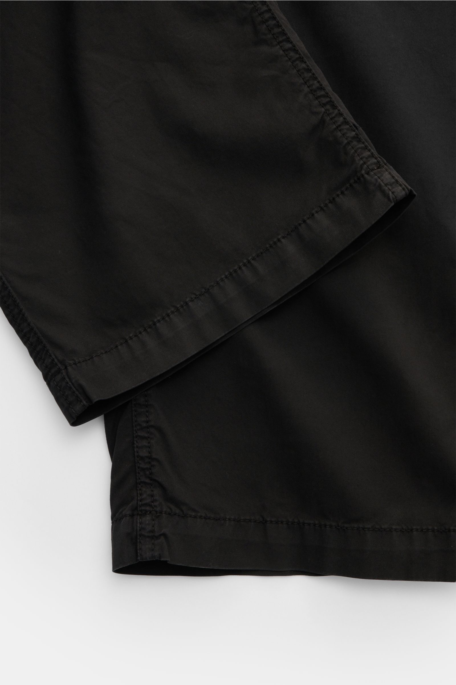 Close-up front view of Stone Island Joggpants schwarz showing black lightweight, slightly elastic cotton fabric with soft touch and neat stitching. Diese leger geschnittene Joggpants aus hochwertiger, leicht elastischer Baumwolle von STONE ISLAND hat mit 