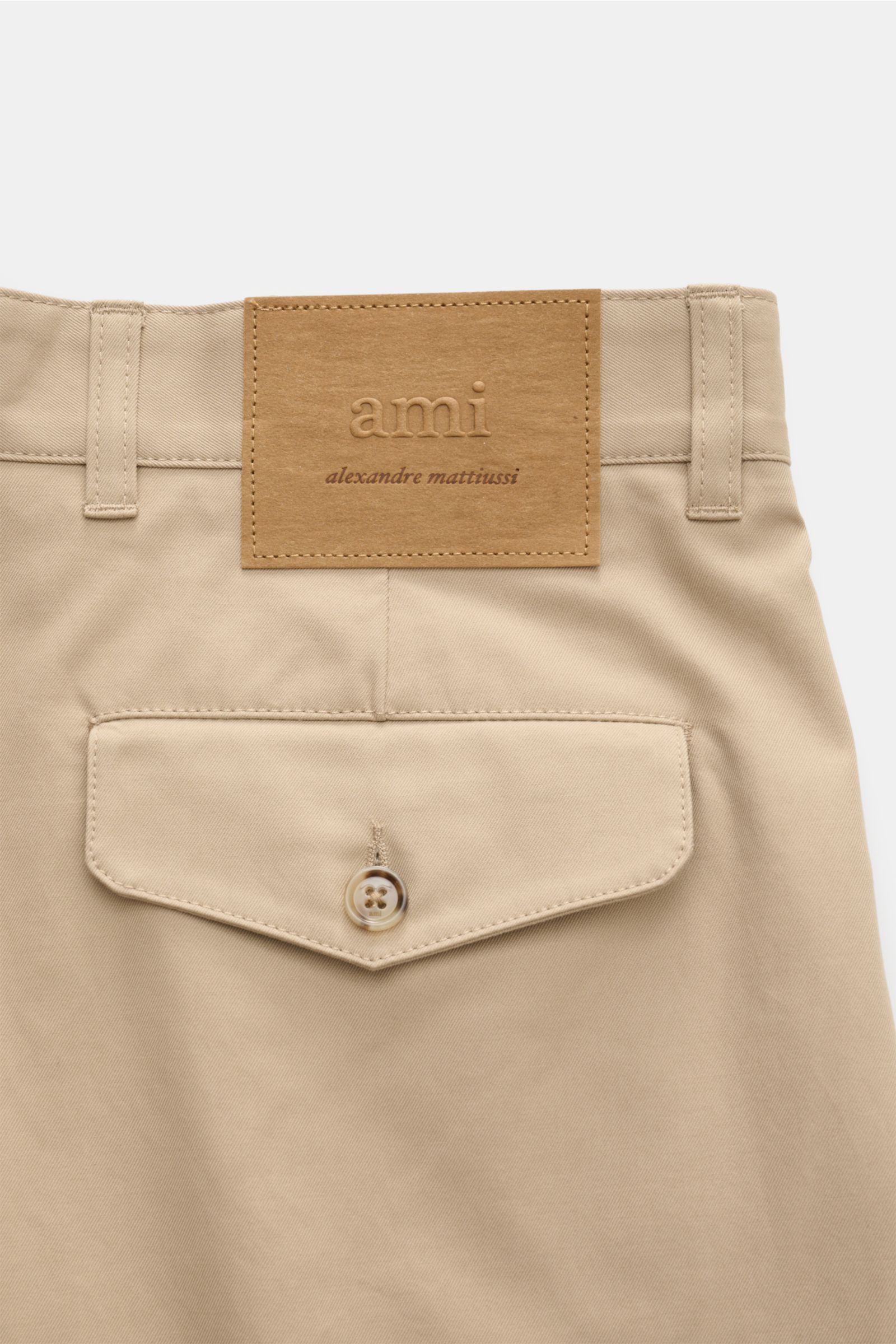 Close-up rear view of Ami Paris Baumwollhose beige showing pure cotton fabric, smooth texture, tapered fit, regular thigh width, ankle length, button fly and waistband button, back pocket with button, and vegan leather patch with 'ami alexandre mattiussi'
