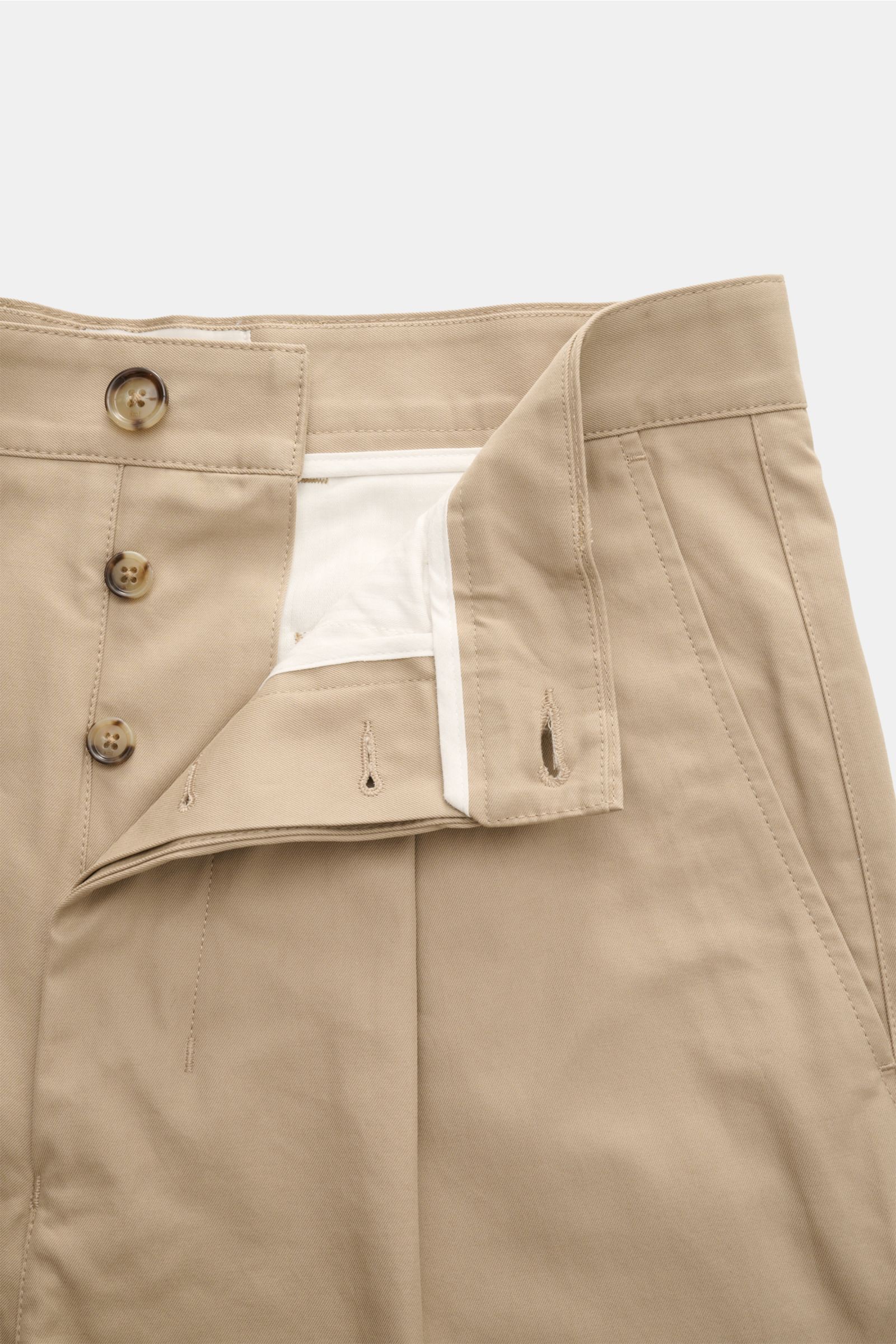 Close-up front view of Ami Paris Baumwollhose beige, showing button fly and waistband with button, pure cotton fabric with smooth touch, tapered fit, regular thigh width, ankle-length design, buttoned back pockets, and vegan leather patch.